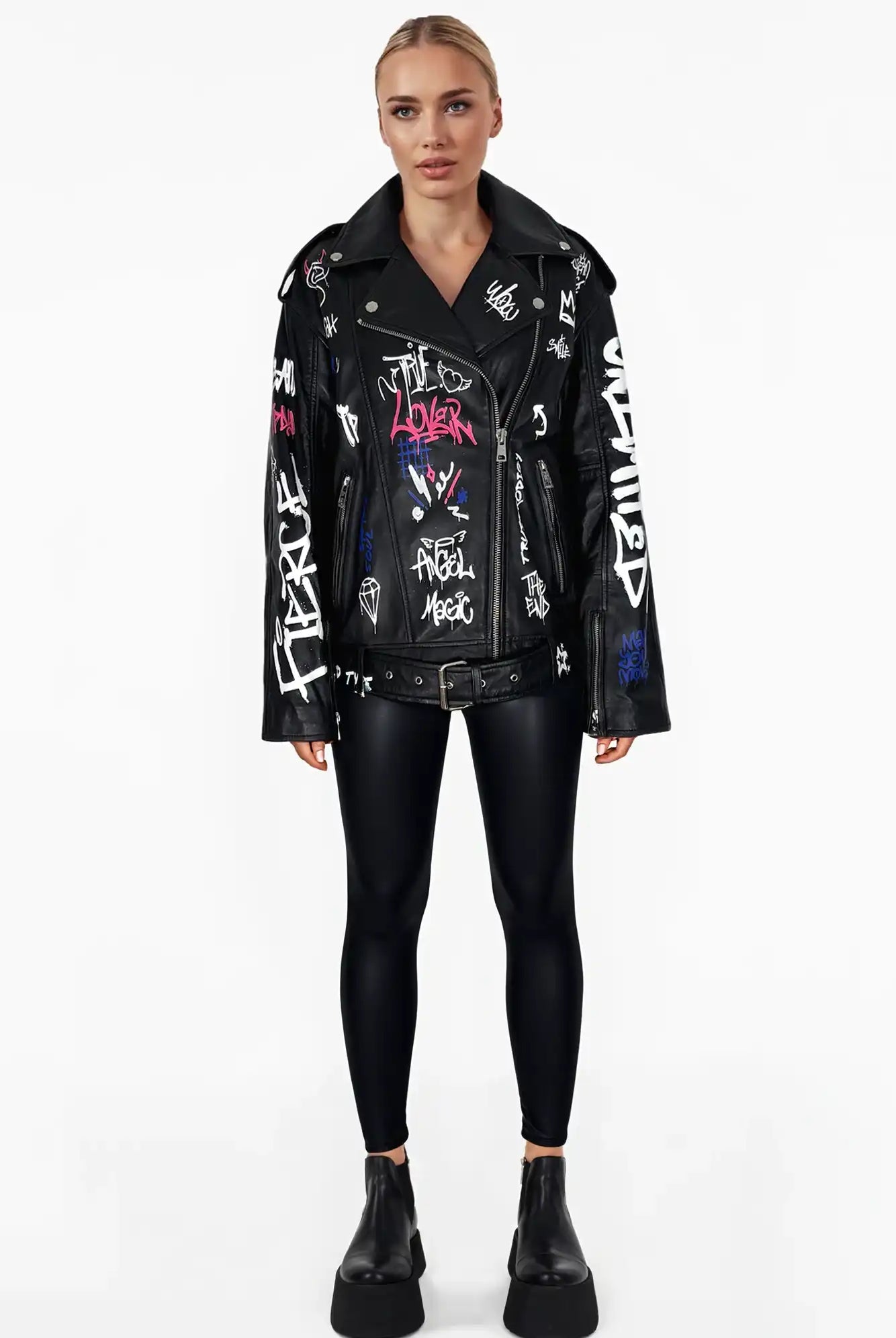 Eine Frau mit blondem Haar steht mit Blick nach vorne in der Anya Schafsleder Jacke von trueprodigy im schwarzen Graffiti-Stil, gepaart mit schwarzen Leggings und Plateaustiefeln vor einem schlichten weißen Hintergrund.