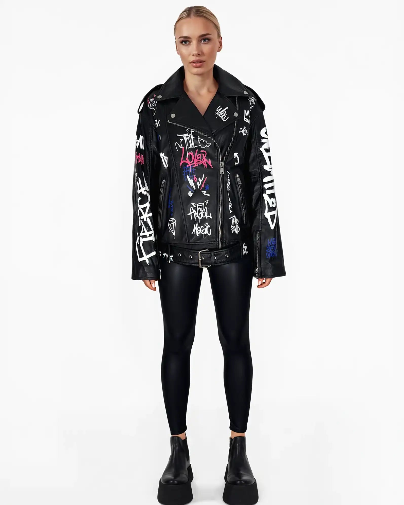 Eine Frau mit blondem Haar steht mit Blick nach vorne in der Anya Schafsleder Jacke von trueprodigy im schwarzen Graffiti-Stil, gepaart mit schwarzen Leggings und Plateaustiefeln vor einem schlichten weißen Hintergrund.