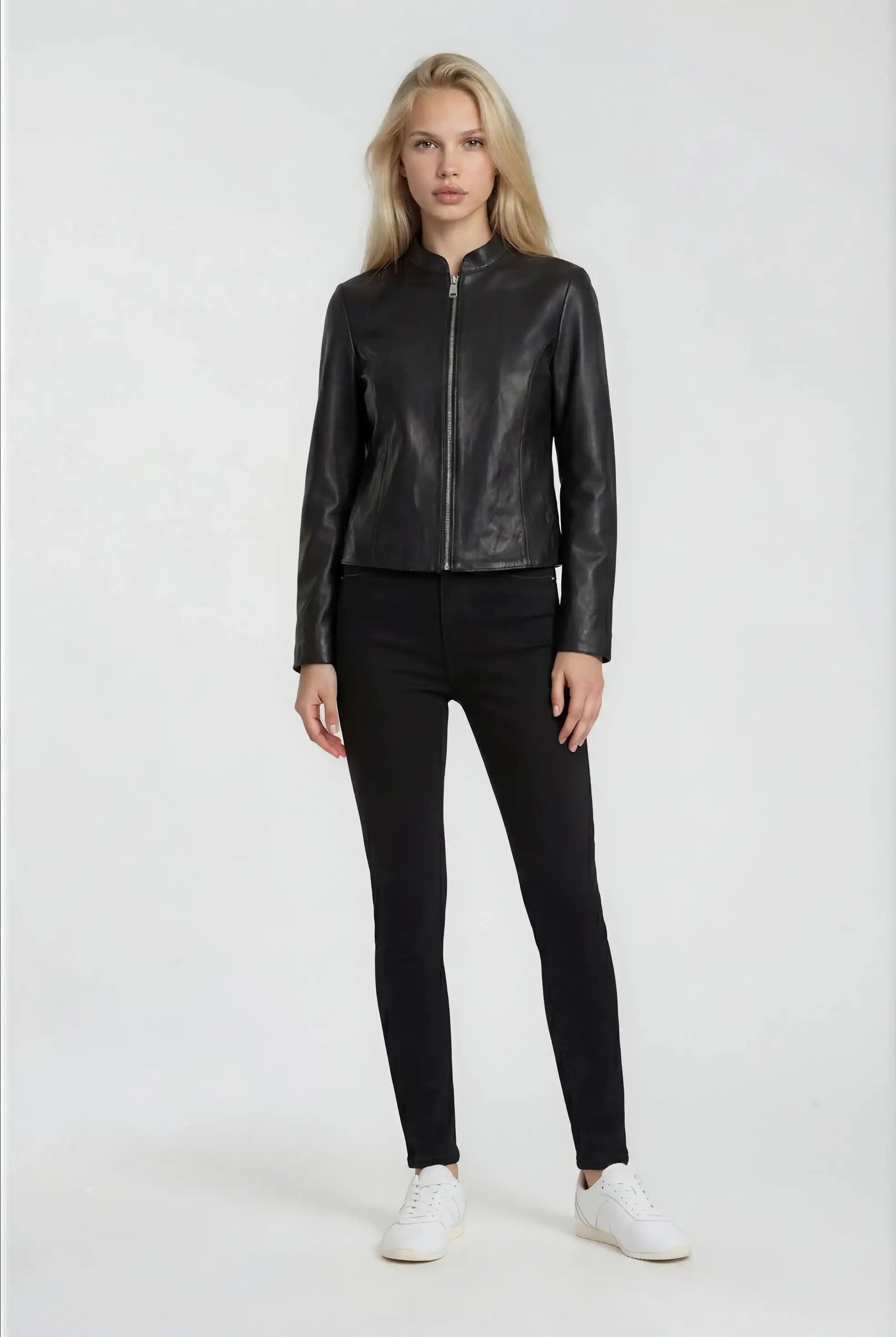 Eine Frau trägt die trueprodigy Damen Lederjacke aus Schafsleder in Schwarz mit minimalistischem Design, dazu schwarze Hose und weiße Sneaker. Sie hat lange blonde Haare und steht vor weißem Hintergrund.