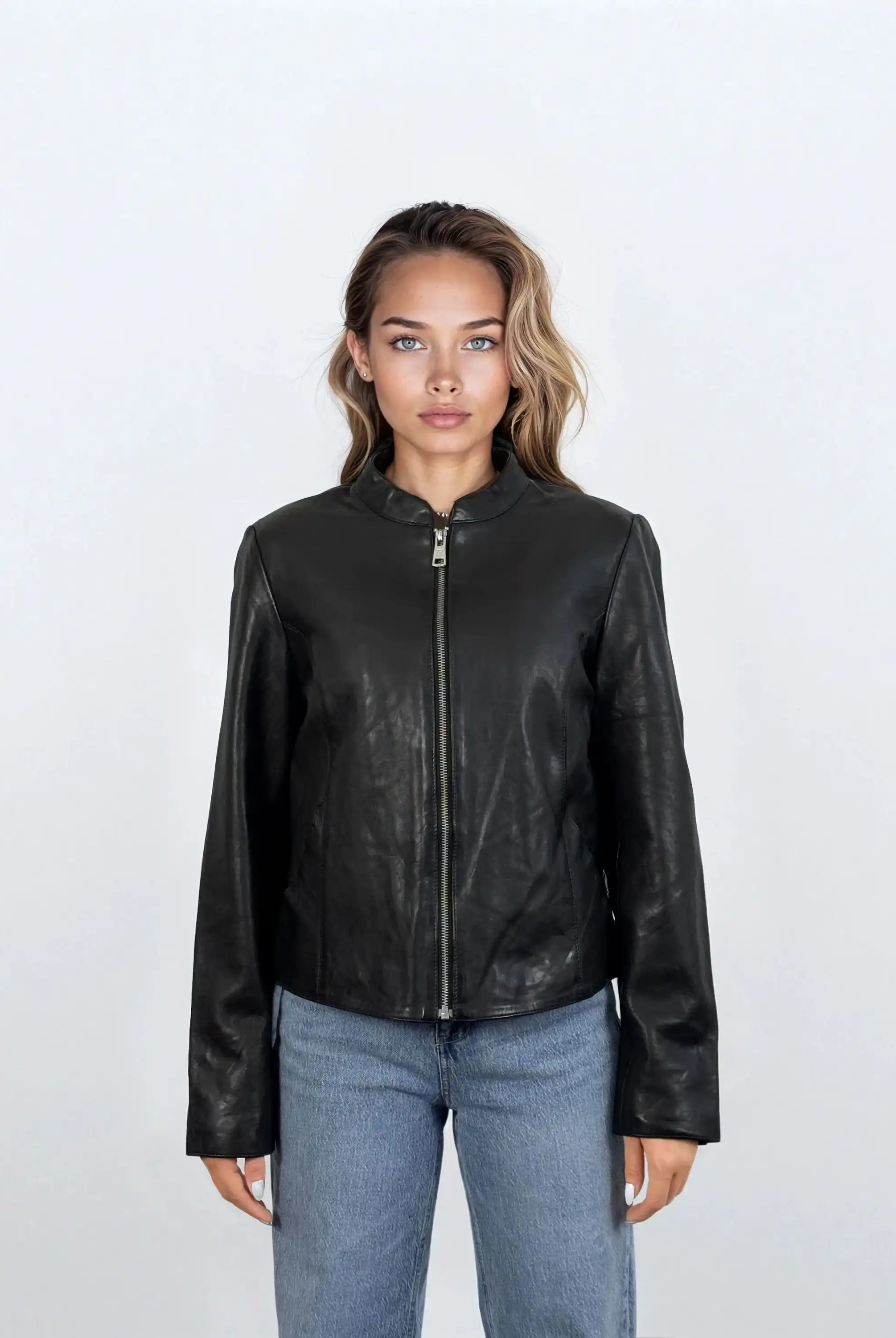 Eine Person mit hellbraunem Haar, die die trueprodigy Damen Lederjacke aus Schafsleder in Schwarz mit minimalistischem Design und Blue Jeans trägt, steht mit dem Gesicht nach vorne vor einem schlichten weißen Hintergrund.