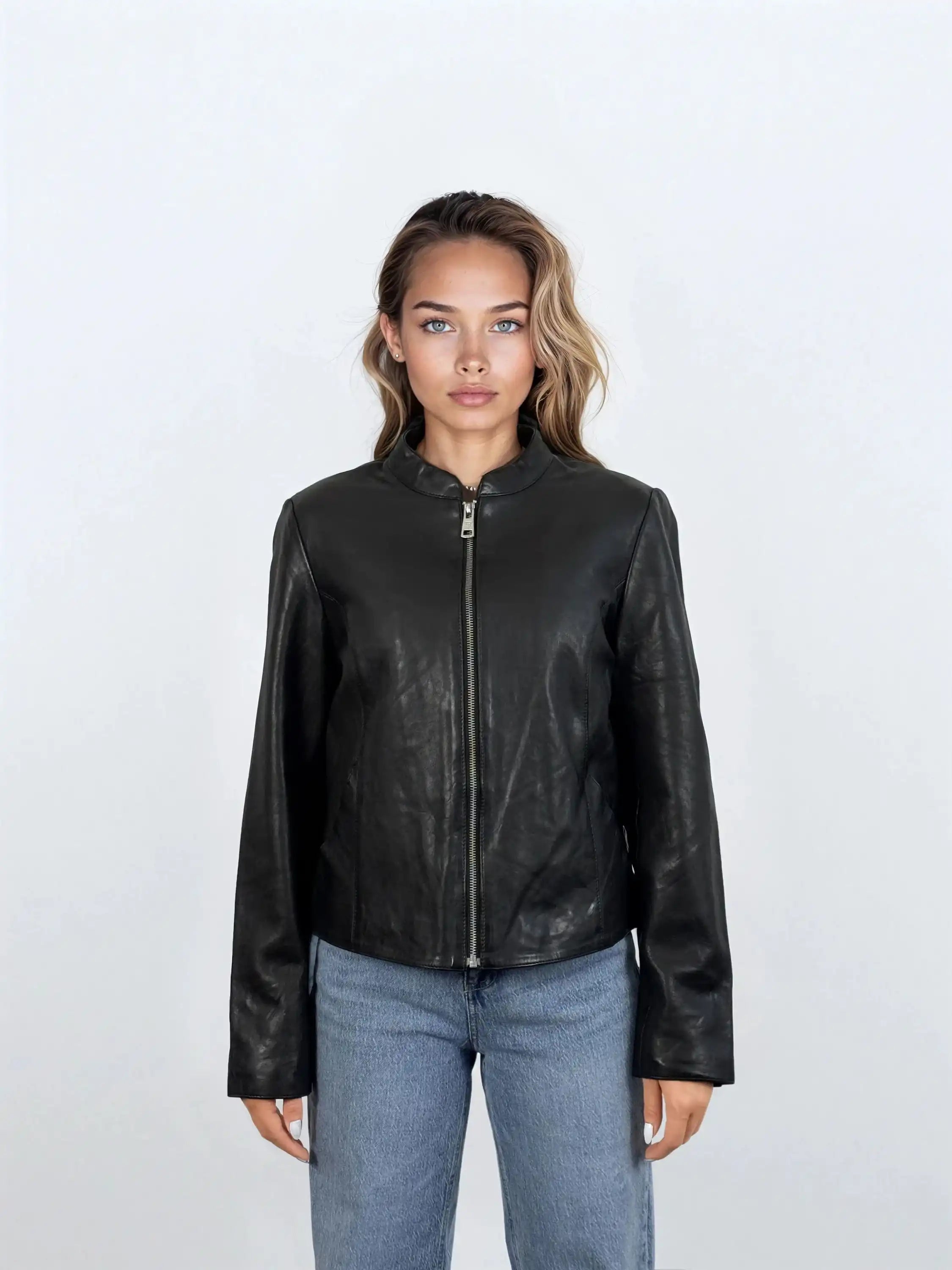 Eine Person mit hellbraunem Haar, die die trueprodigy Damen Lederjacke aus Schafsleder in Schwarz mit minimalistischem Design und Blue Jeans trägt, steht mit dem Gesicht nach vorne vor einem schlichten weißen Hintergrund.