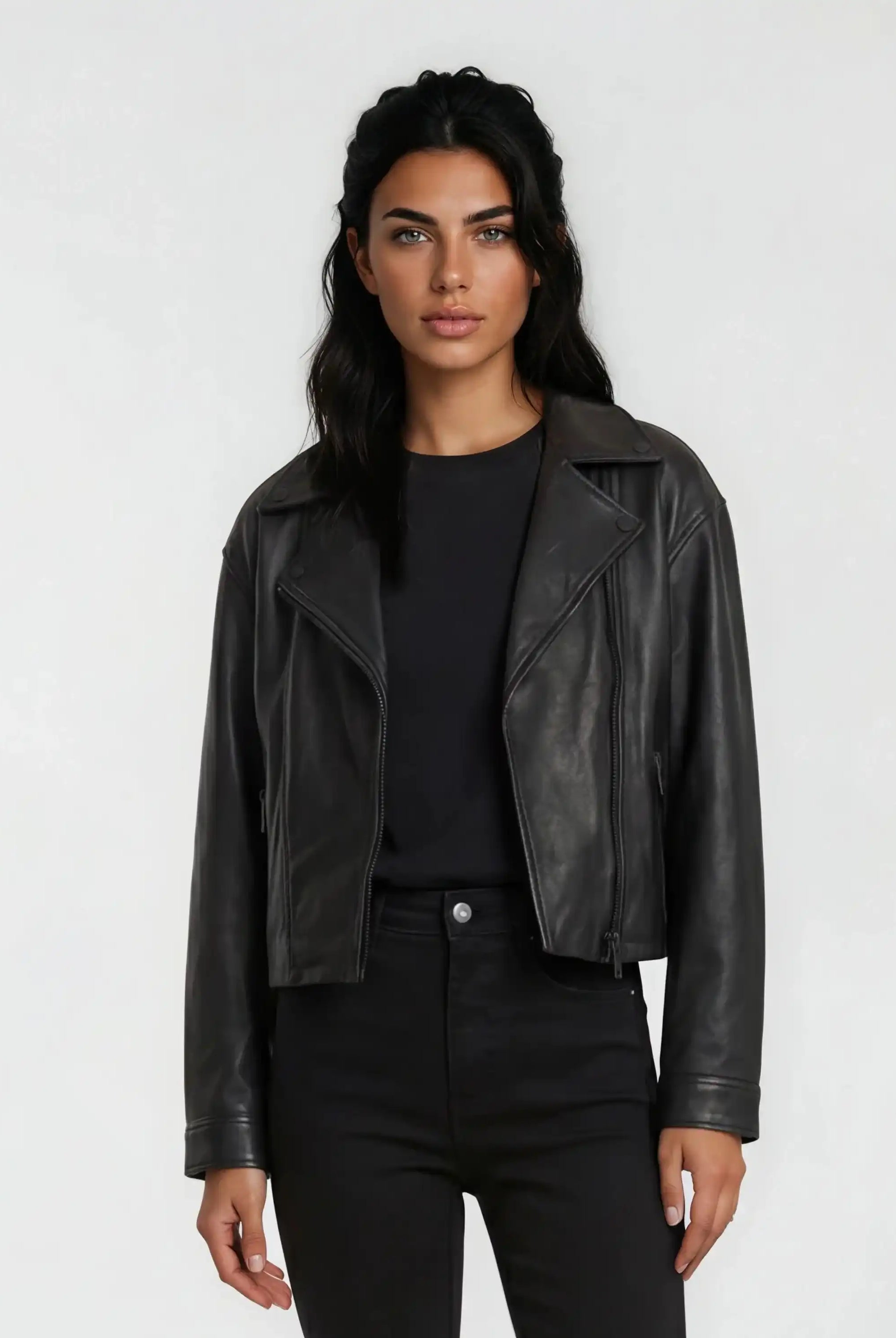 Eine Frau mit langen dunklen Haaren trägt die trueprodigy Damen Lederjacke aus Schafsleder in Schwarz im Oversized Cropped-Style über einem schwarzen Hemd und einer Hose und steht mit dem Gesicht nach vorne vor einem schlichten hellen Hintergrund.