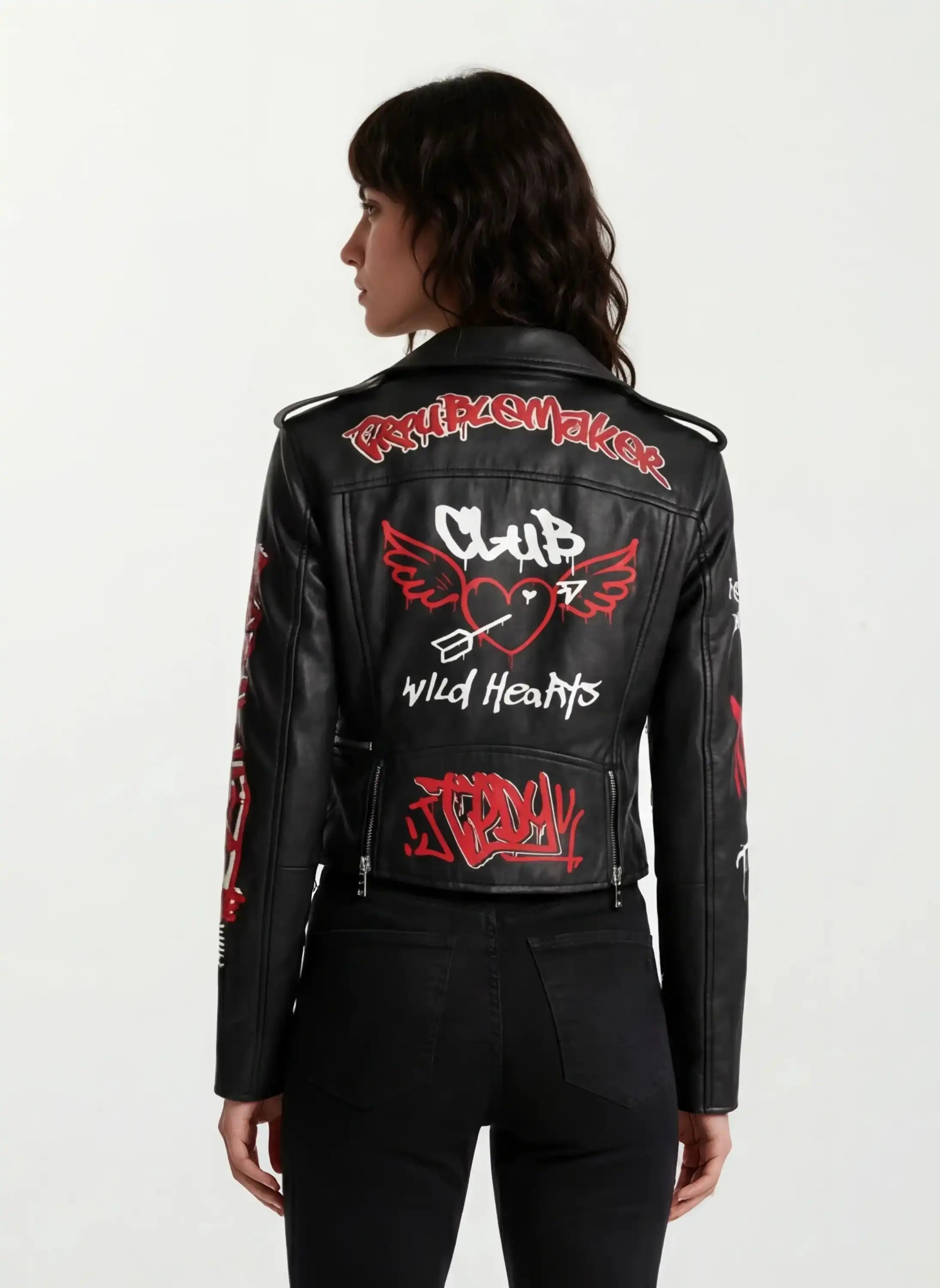 Eine Frau mit mittellangen dunklen Haaren ist von hinten zu sehen. Sie trägt die trueprodigy Feminine Lederjacke mit Grafittiprint und Reißverschluss, eine schwarze Lederjacke mit roten und weißen Graffiti-Grafiken und Text.