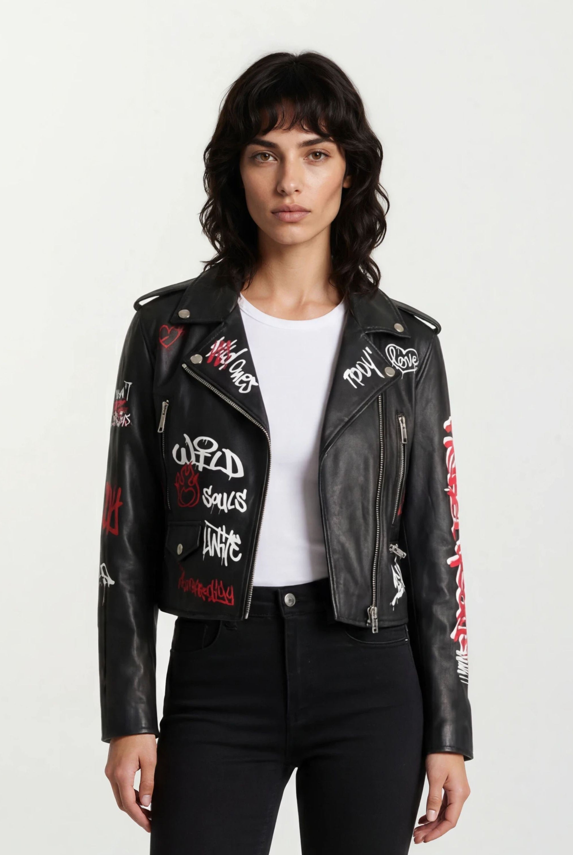 Eine Person mit schulterlangen dunklen Haaren trägt die trueprodigy Feminine Lederjacke mit Grafittiprint und Reißverschluss über einem schlichten weißen T-Shirt und steht vor einem schlichten hellen Hintergrund.