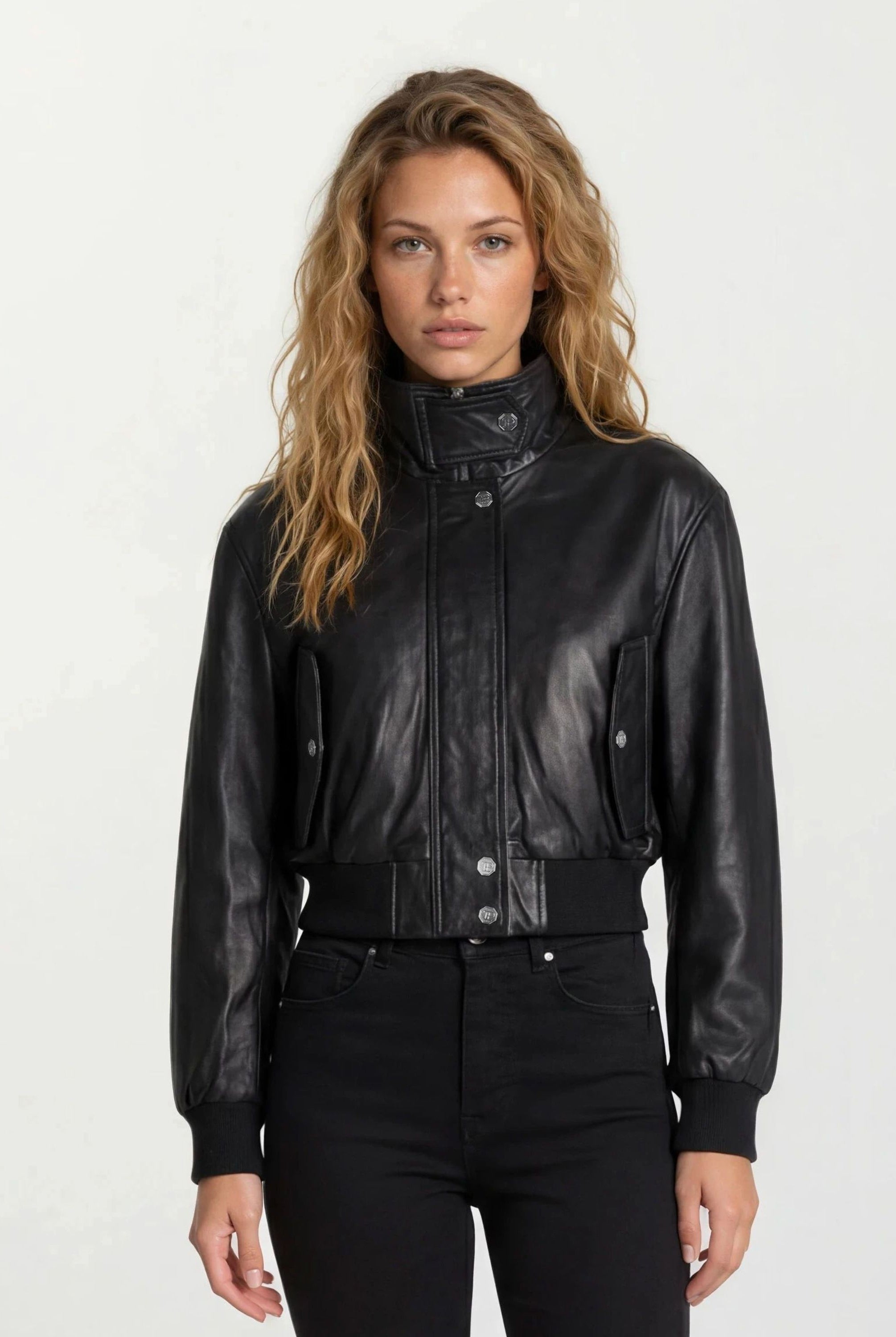 Eine Frau mit gewelltem, hellbraunem Haar trägt die trueprodigy Feminine Lederjacke Stehkragen und Reißverschluss und eine schwarze Hose und steht vor einem schlichten, hellen Hintergrund.