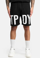 Eine Person trägt die trueprodigy Walden Sweatshort mit Print mit großen weißen Buchstaben TPY und DY, gepaart mit weißen Crew-Socken und Sneakers, vor einem schlichten hellen Hintergrund. Diese Shorts bieten einen modernen Schnitt für einen trendigen Look.