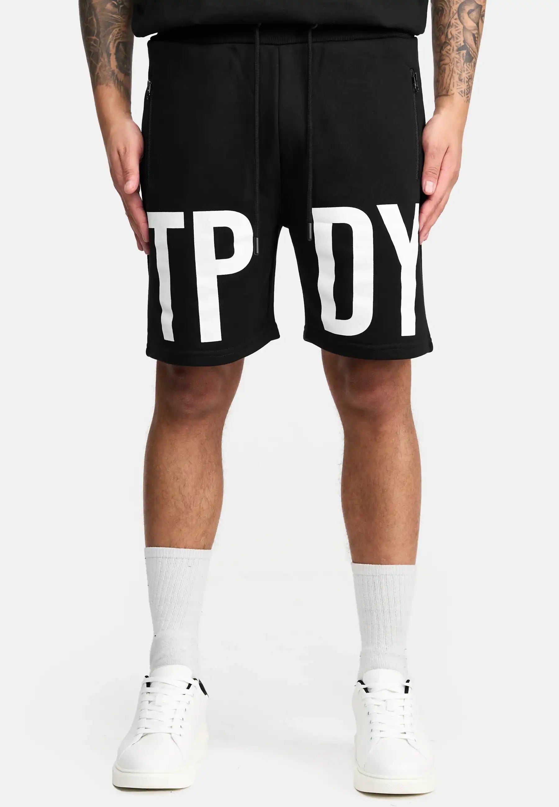 Eine Person trägt die trueprodigy Walden Sweatshort mit Print mit großen weißen Buchstaben TPY und DY, gepaart mit weißen Crew-Socken und Sneakers, vor einem schlichten hellen Hintergrund. Diese Shorts bieten einen modernen Schnitt für einen trendigen Look.