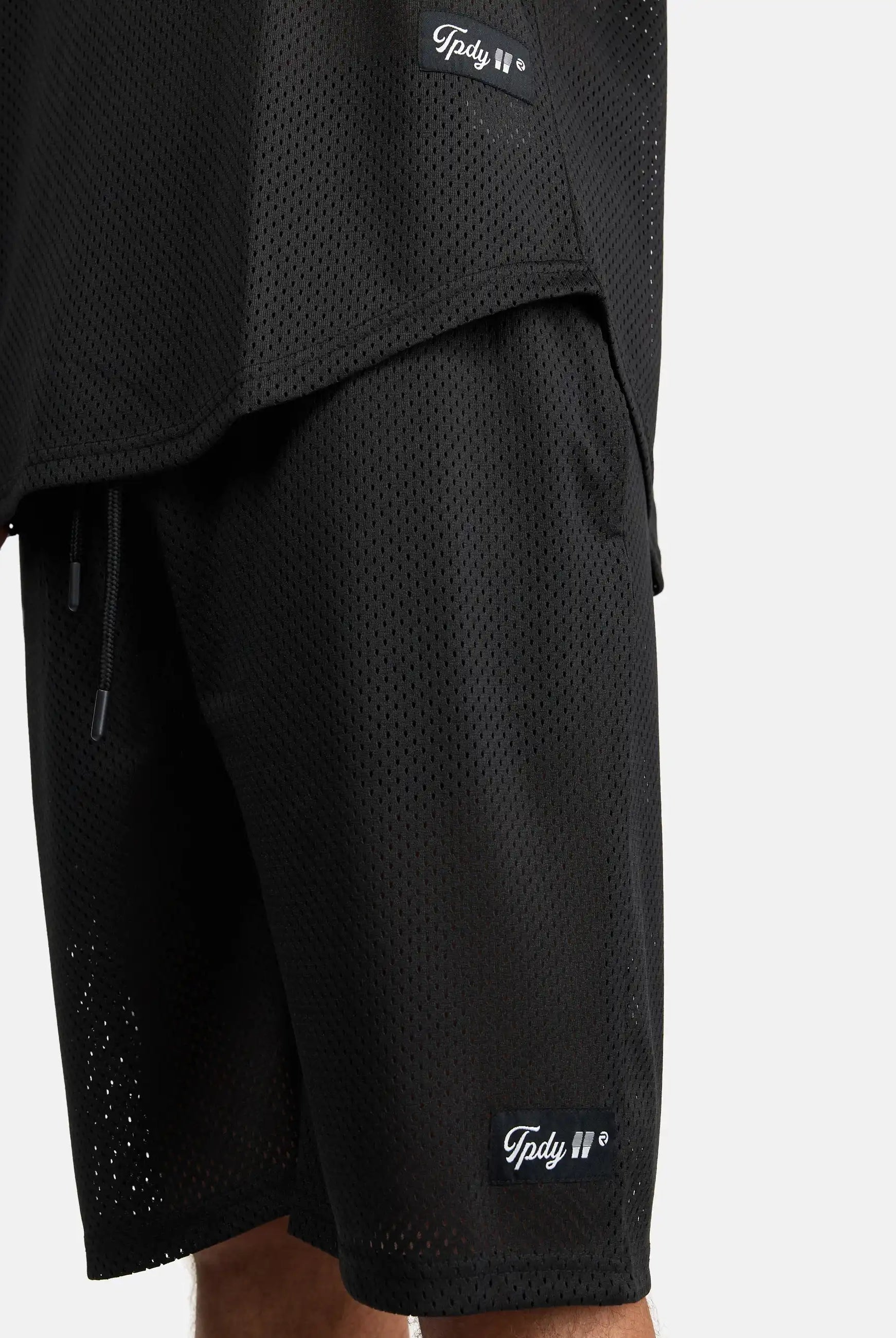 Nahaufnahme einer Person, die die Allen Short aus Mesh und das dazu passende schwarze Mesh-Top von trueprodigy trägt, beide mit kleinen rechteckigen Markenetiketten an den Säumen. Der Hintergrund ist einfarbig weiß.