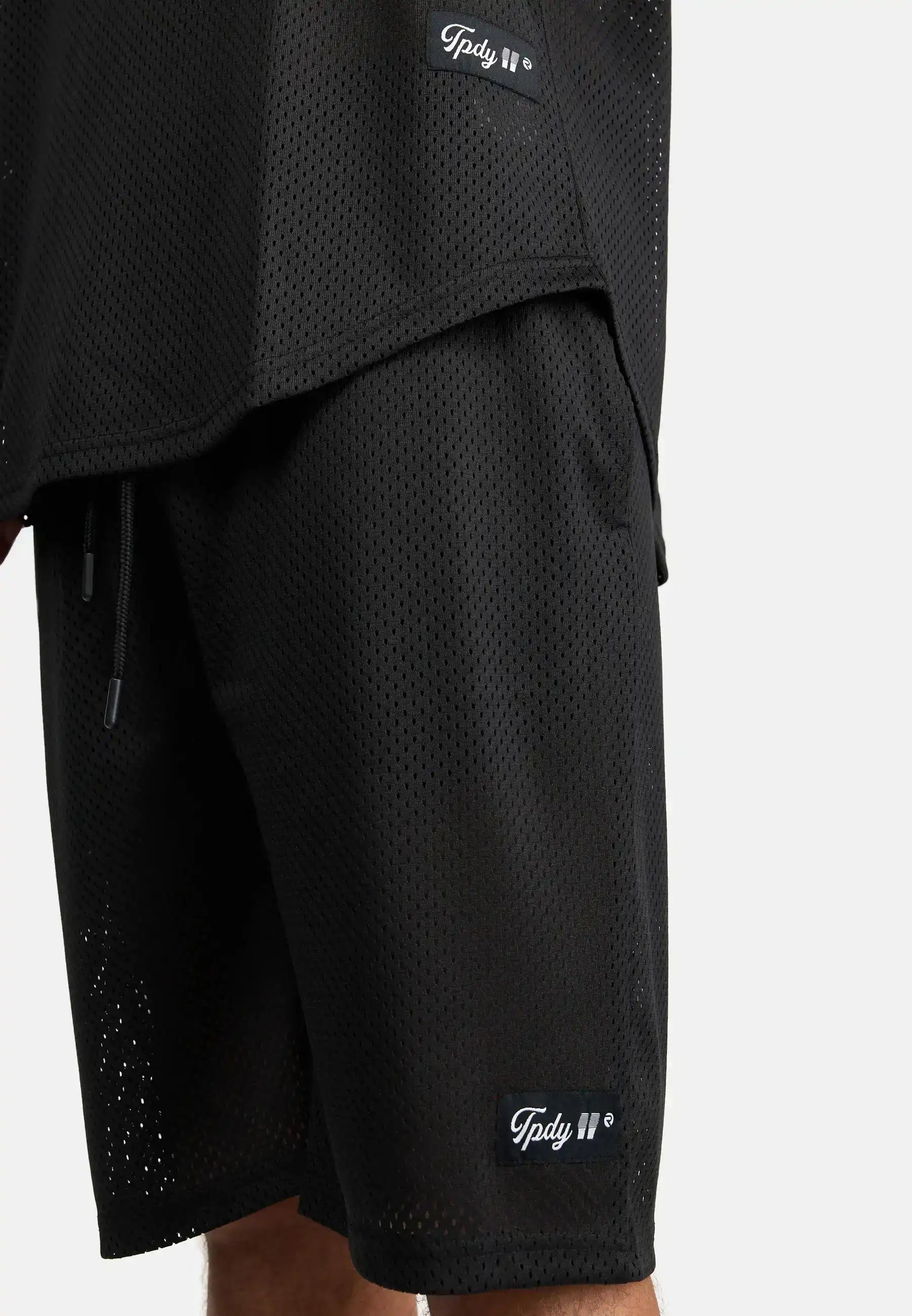 Nahaufnahme einer Person, die die Allen Short aus Mesh und das dazu passende schwarze Mesh-Top von trueprodigy trägt, beide mit kleinen rechteckigen Markenetiketten an den Säumen. Der Hintergrund ist einfarbig weiß.