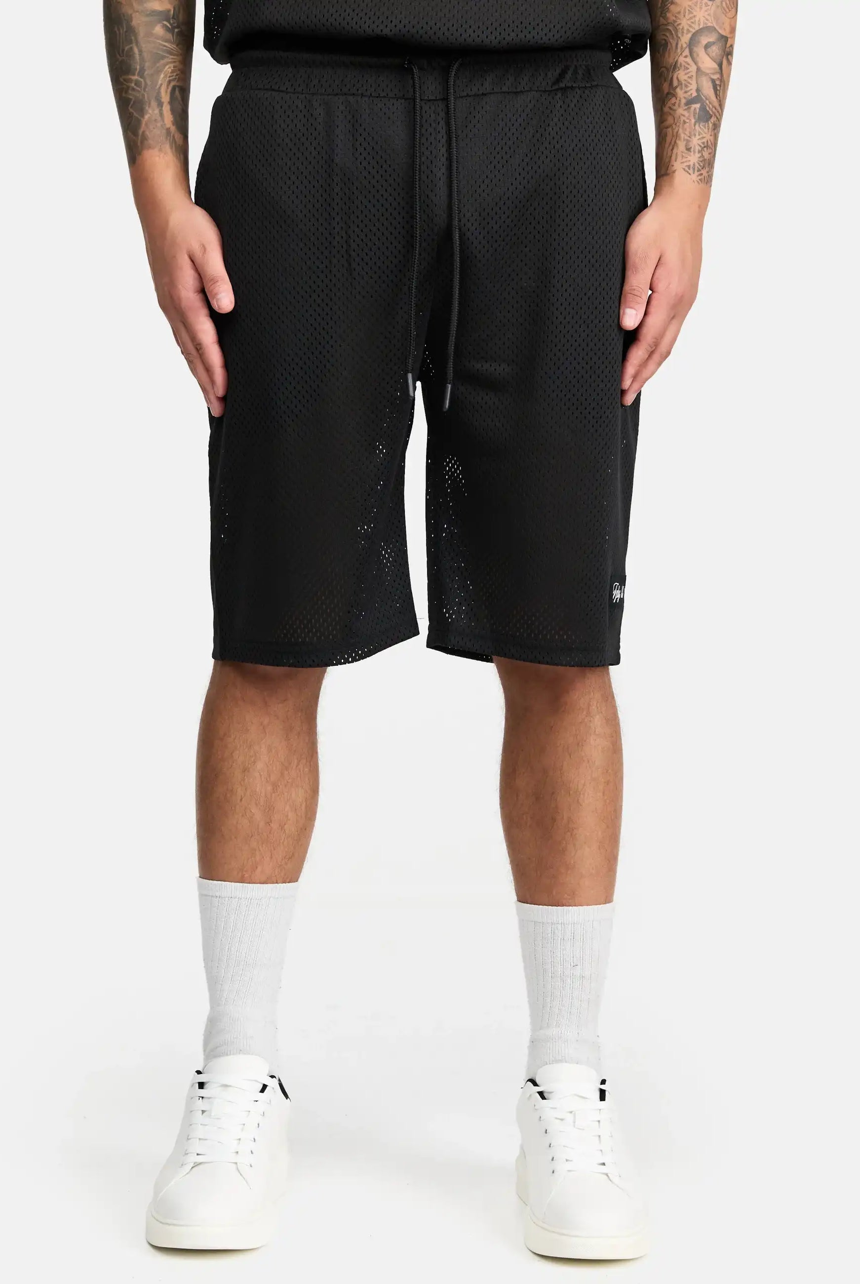 Eine Person, die trueprodigy Allen Short aus Mesh, weiße Socken und weiße Turnschuhe trägt, steht vor einem schlichten weißen Hintergrund. Nur der untere Teil des Oberkörpers und die Beine sind zu sehen, mit Tätowierungen auf beiden Unterarmen.