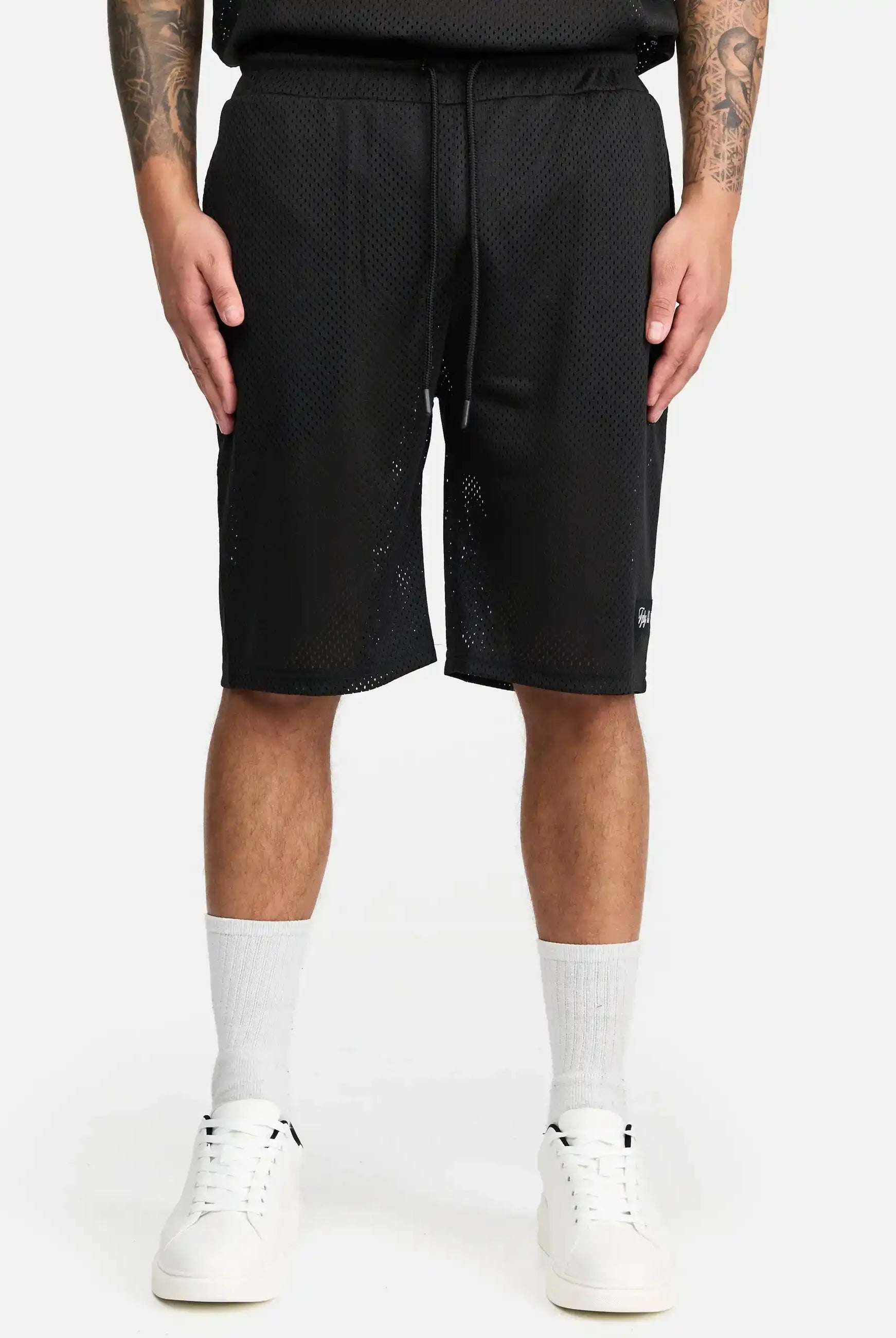 Eine Person, die trueprodigy Allen Short aus Mesh, weiße Socken und weiße Turnschuhe trägt, steht vor einem schlichten weißen Hintergrund. Nur der untere Teil des Oberkörpers und die Beine sind zu sehen, mit Tätowierungen auf beiden Unterarmen.