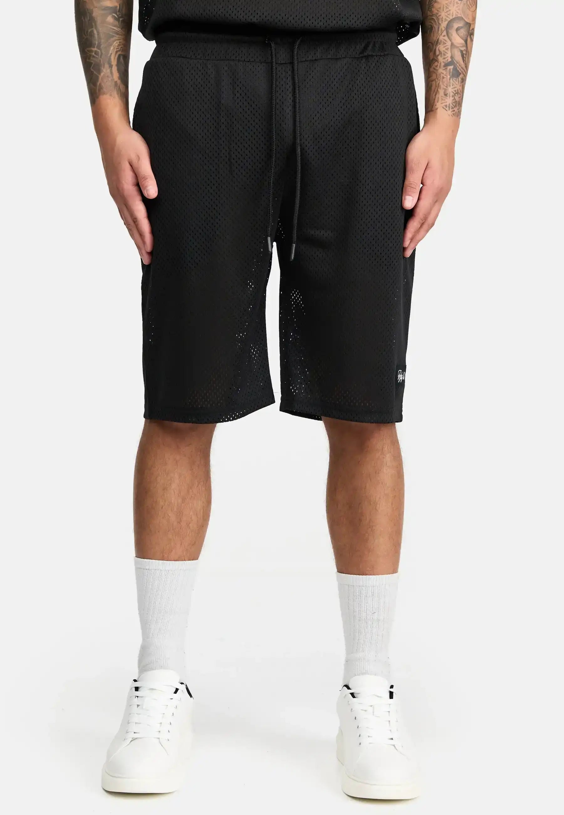 Eine Person, die trueprodigy Allen Short aus Mesh, weiße Socken und weiße Turnschuhe trägt, steht vor einem schlichten weißen Hintergrund. Nur der untere Teil des Oberkörpers und die Beine sind zu sehen, mit Tätowierungen auf beiden Unterarmen.