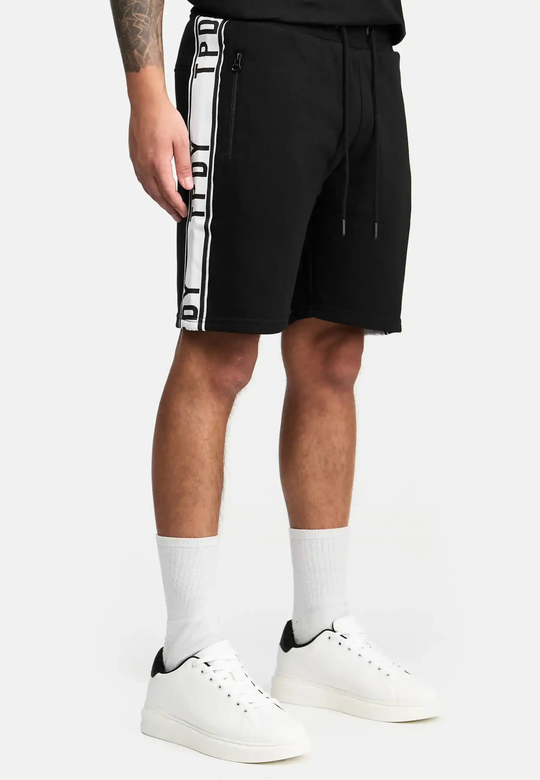 Eine Person trägt trueprodigy Benjamin Logo Shorts mit Reißverschlusstaschen und einem Kordelzug in der Taille, gepaart mit weißen Socken und Turnschuhen. Nur die untere Hälfte des Körpers ist vor einem einfarbigen Hintergrund zu sehen.
