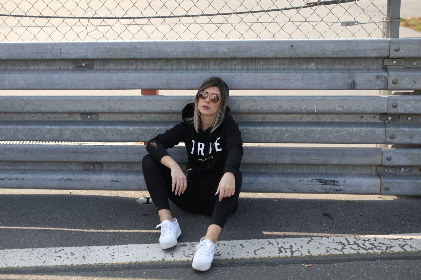 Damenmodel mit Sweater sitzend vor Leitplanke auf Rennbahn