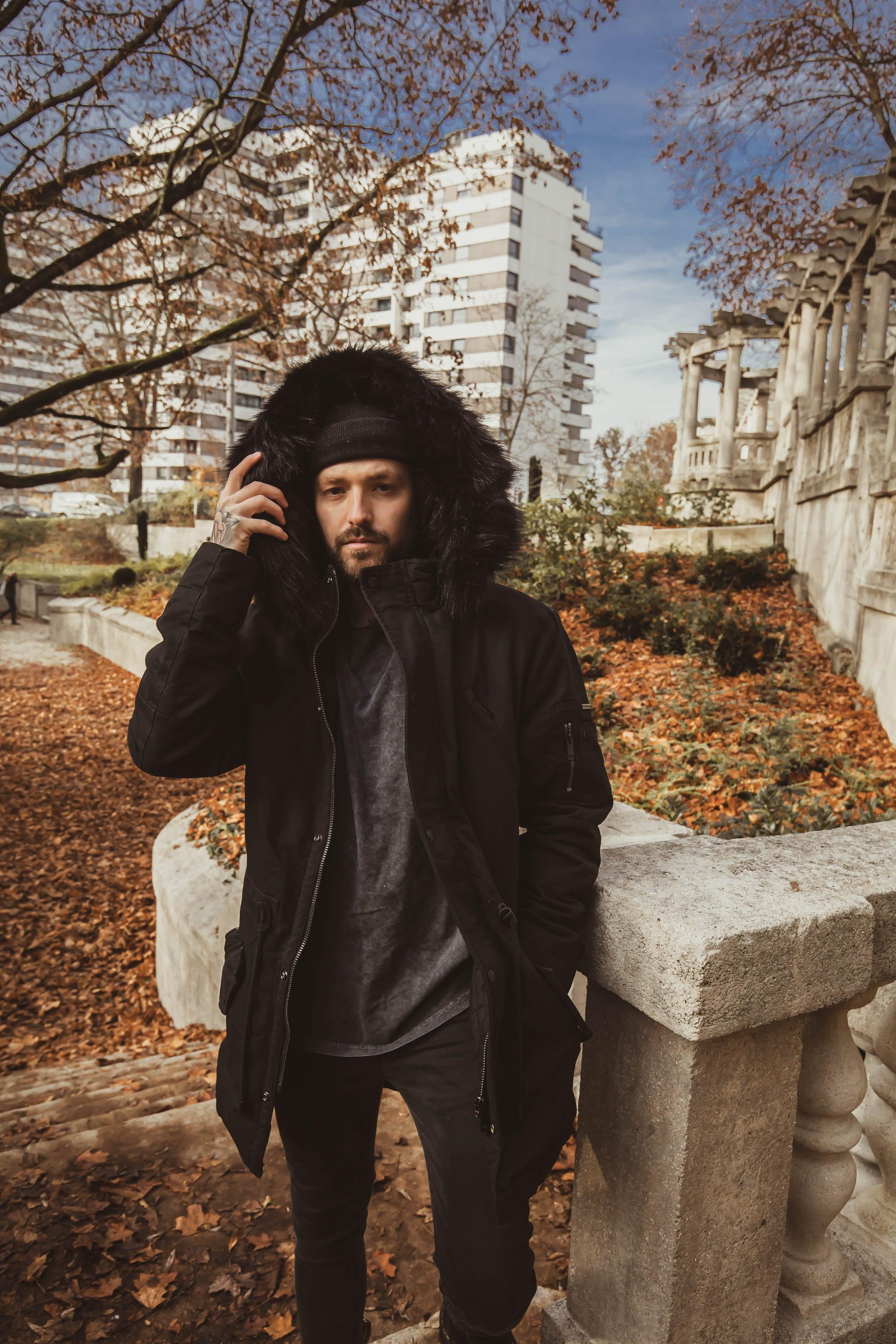 Herren Model im Vordergund mit offener Winterjacke und Kapuze über Kopf