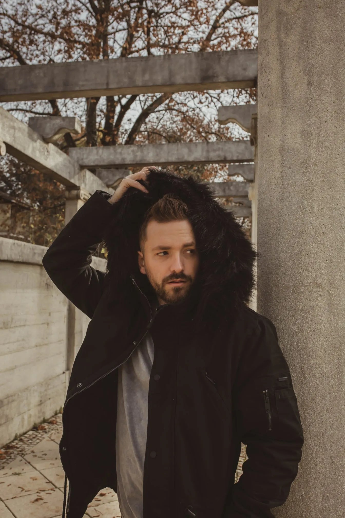 Herrenmodel mit Winterjacke und Kapuze in schwarz vor herbstlichem Hintergrund