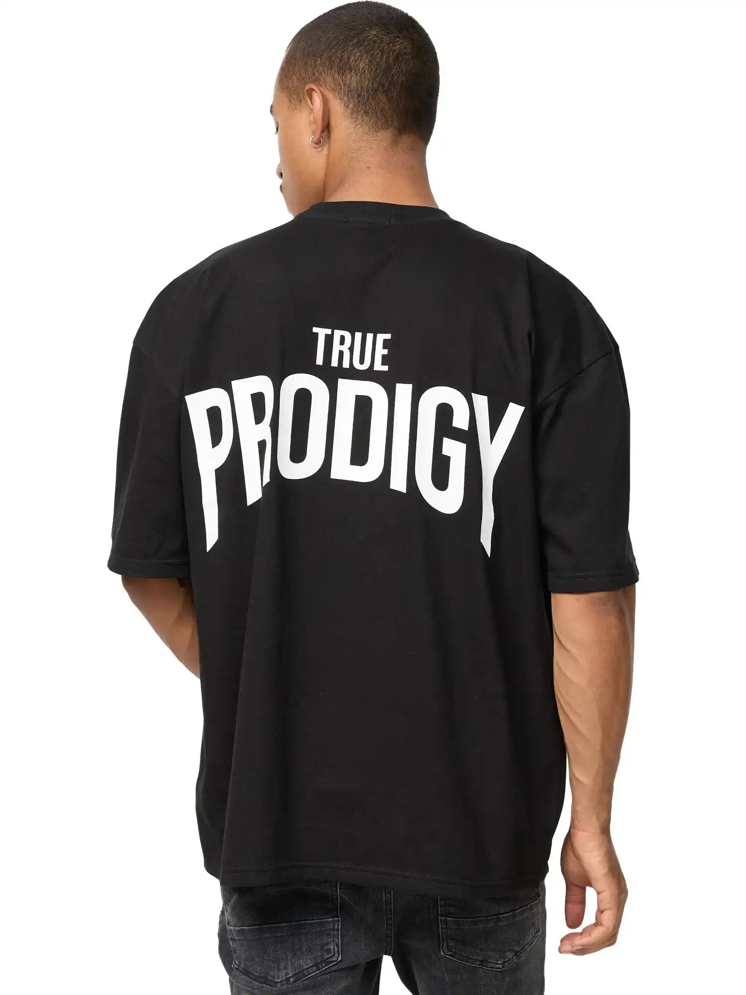 Eine Person blickt von der Kamera weg und trägt das trueprodigy Jona Oversized T-Shirt mit Druck in schwarz mit dem Aufdruck TRUE PRODIGY in fetten weißen Buchstaben auf dem Rücken, gepaart mit einer dunklen Jeans.