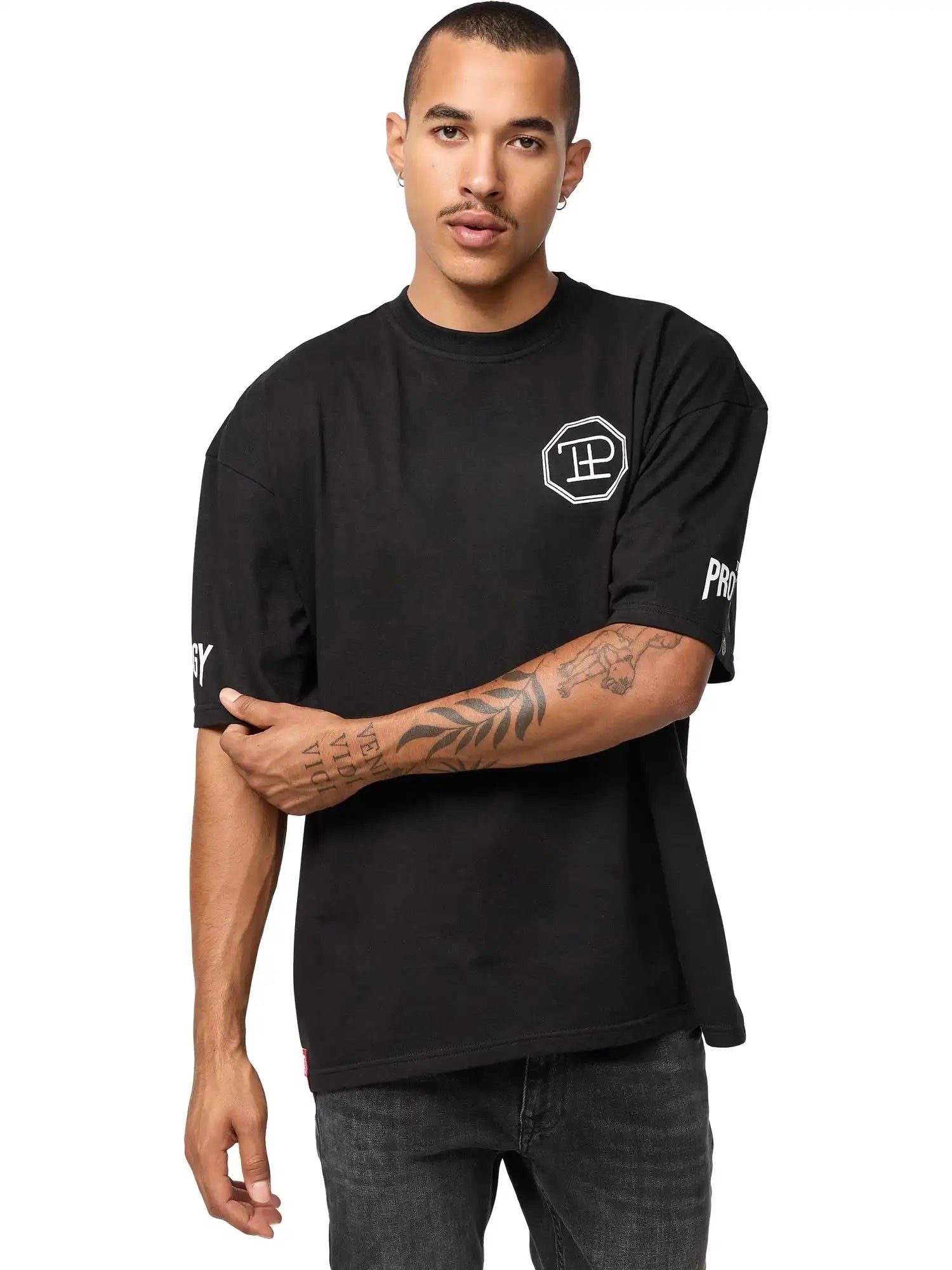Eine Person mit kurzen Haaren und Schnurrbart trägt das trueprodigy Dilan Oversized T-Shirt mit Druck-schwarz, unisex, mit weißen grafischen Prints auf Brust und Ärmeln-gepaart mit dunklen Jeans, vor einem schlichten weißen Hintergrund.