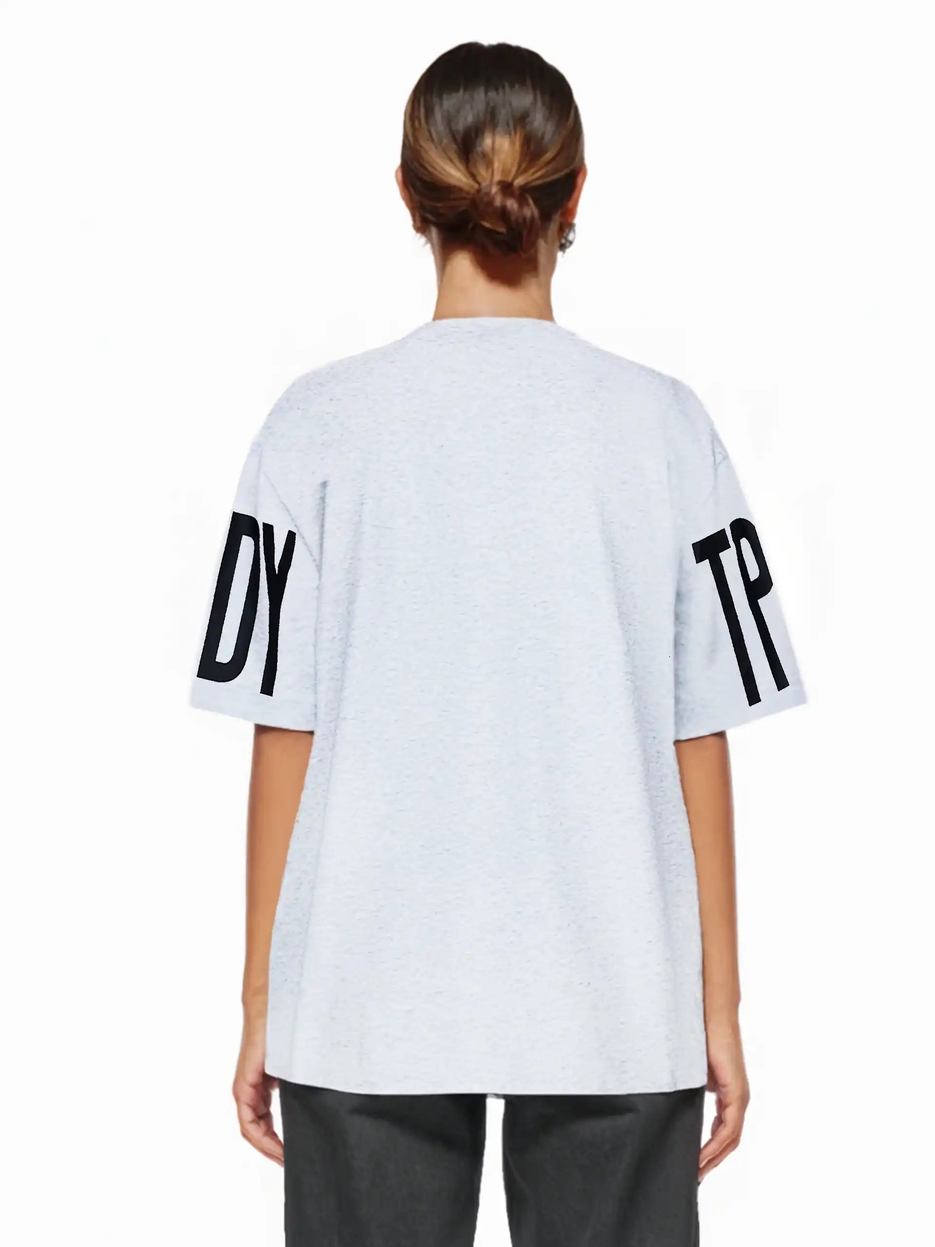 Eine Person steht mit dem Gesicht zur Wand und trägt das Viktor F Oversize-Damen-T-Shirt mit Ärmelprints und Frontprint unter dem Kragen von trueprodigy in Hellgrau, mit großen Ärmeldrucken, gepaart mit einer dunklen Hose. Die Haare sind zu einem tiefen Dutt gestylt.