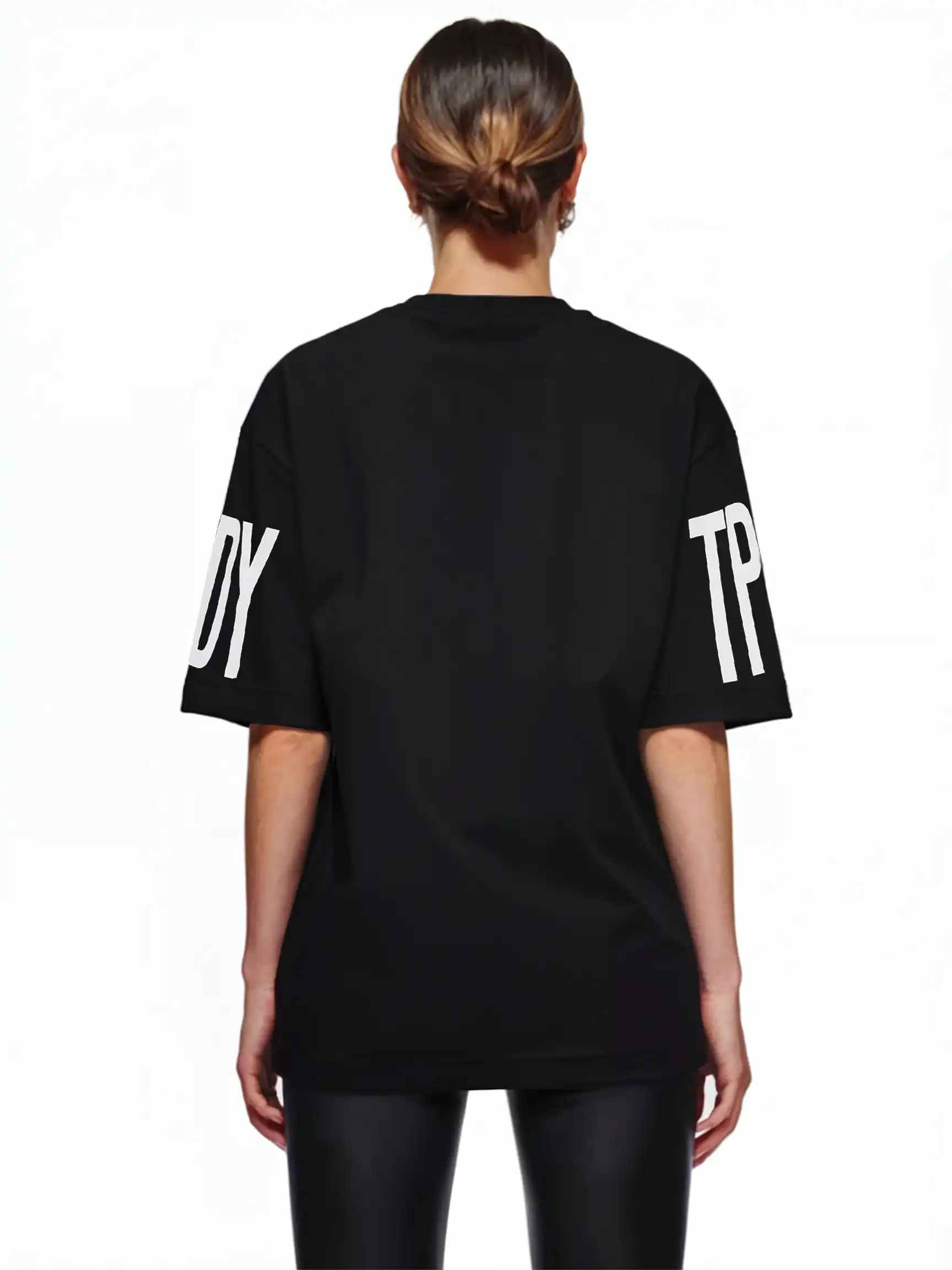 Man sieht eine Person mit braunen Haaren in einem tiefen Dutt von hinten, die das trueprodigy Viktor F Oversize-Damen-T-Shirt mit Ärmelprints und Frontprint unter dem Kragen und eine schwarz glänzende Hose trägt und vor einem weißen Hintergrund steht.
