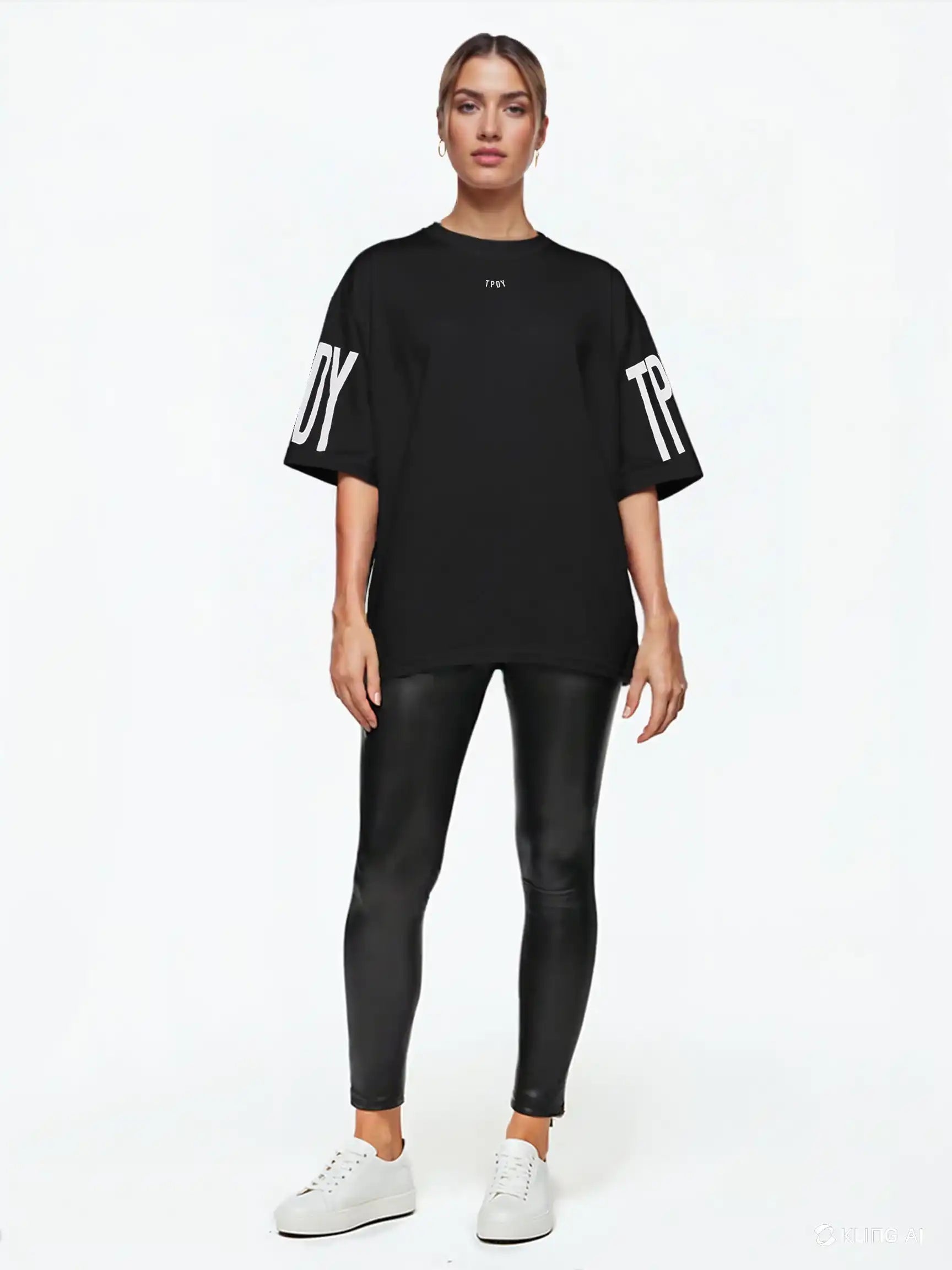 Eine Person blickt nach vorne und trägt das trueprodigy Viktor F Oversize-Damen-T-Shirt mit Ärmelprints und Frontprint unter dem Kragen, gepaart mit schwarzen Leggings in Lederoptik und weißen Sneakers, vor einem schlichten weißen Hintergrund.