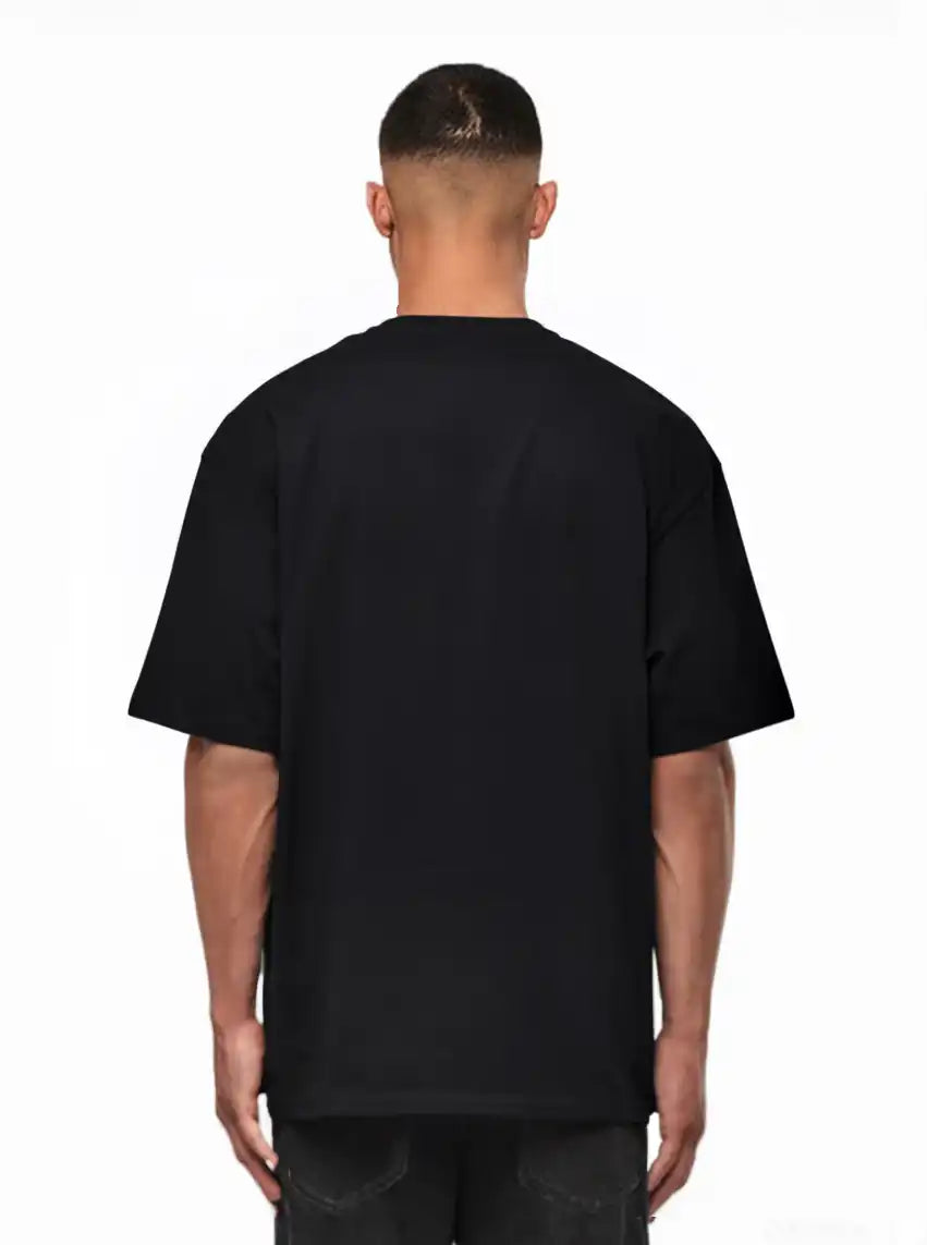 Ein Mann schaut von der Kamera weg, trägt ein schwarzes trueprodigy Noa Oversize-Shirt mit "FEAR NOTHING"-Print & handschriftlichem Detail und dunkle Jeans, vor einem weißen Hintergrund.