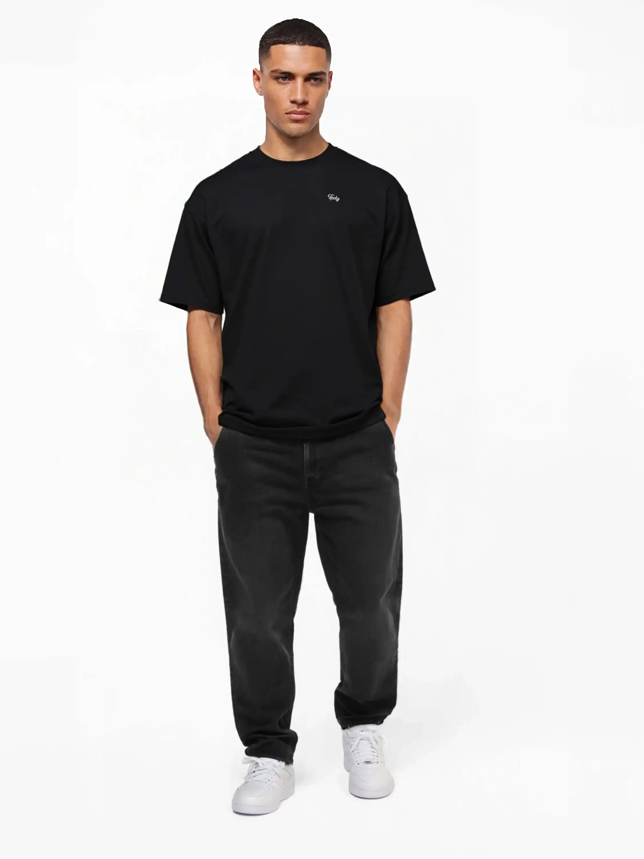 Ein Mann steht mit dem Gesicht nach vorne, die Hände in den Taschen, und trägt das trueprodigy Nika Oversize-Basicshirt mit TPDY-Stickerei & klarer Silhouette mit dunklen Jeans und weißen Turnschuhen vor einem schlichten weißen Hintergrund.
