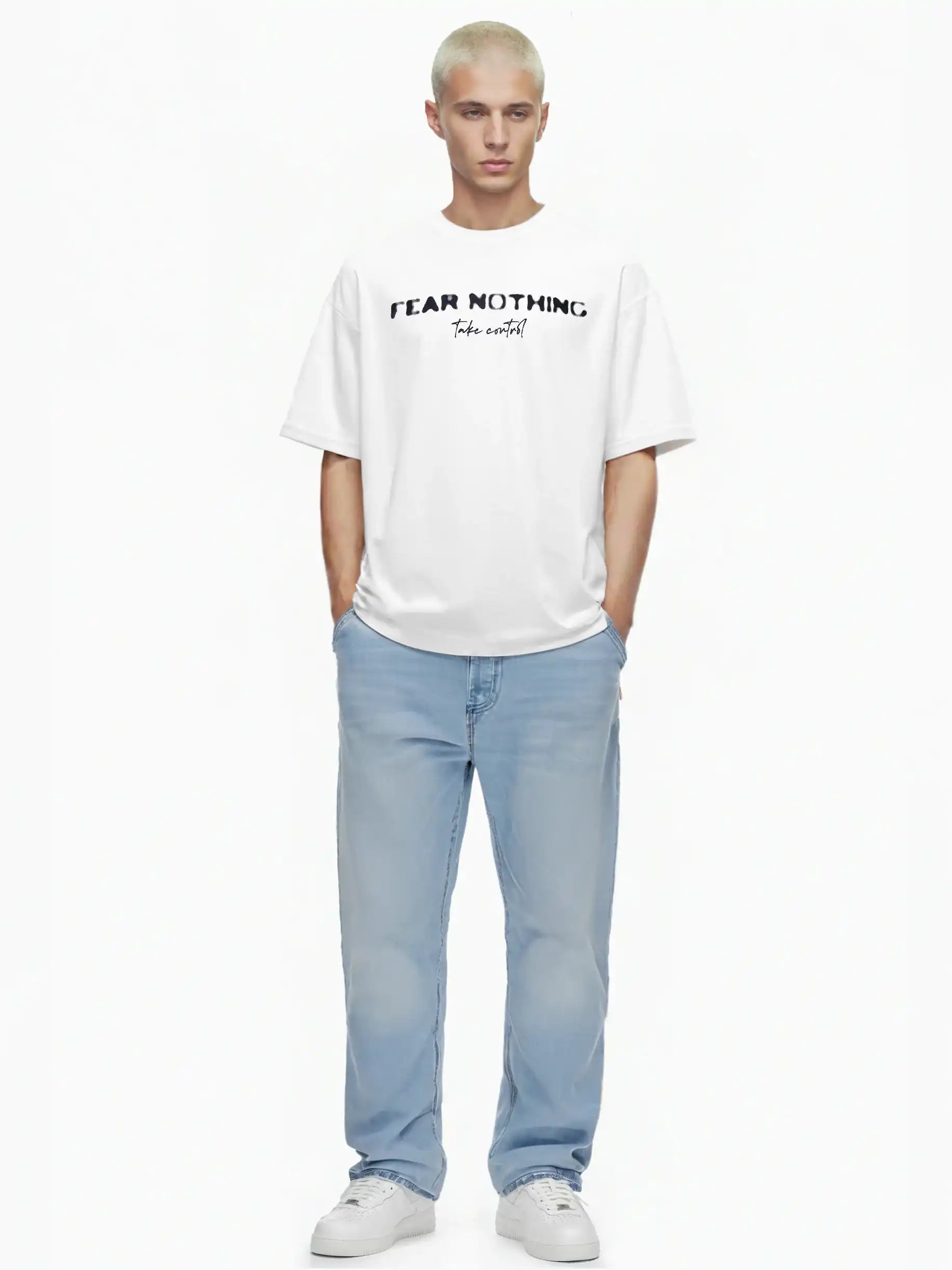 Eine Person mit kurzen blonden Haaren steht vor einem weißen Hintergrund, trägt das trueprodigy Noa Oversize-Shirt mit "FEAR NOTHING"-Print & handschriftlichem Detail, hellblaue Jeans und weiße Turnschuhe. Die Hände stecken in den Taschen.