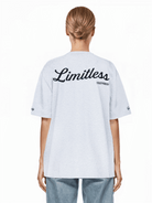 Eine Person mit blonden Haaren zu einem Dutt trägt ein übergroßes weißes „Kai F“ Trueprodigy Unisex-T-Shirt und hellblaue Jeans. Die Rückseite des Shirts aus schwerem Jerseystoff hebt sich vor einem schlichten weißen Hintergrund ab.