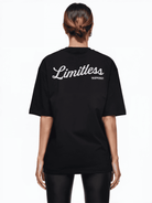Eine Person mit braunen Haaren blickt abgewandt und trägt ein übergroßes schwarzes Trueprodigy Kai F T-Shirt mit „Limitless“-Logoprint auf dem Rücken und eine schwarze Hose. Der schlichte weiße Hintergrund unterstreicht die starke Aussage dieses Unisex-T-Shirts.