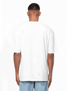 Das Bild zeigt die Rückseite einer Person, die das Ravi-T-Shirt von trueprodigy trägt, kombiniert mit hellblauen Jeans. Sie hat kurze, kurz geschnittene Haare und steht vor einem weißen Hintergrund.
