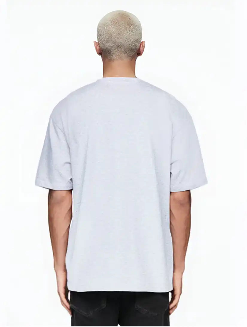 Gezeigt wird eine Person mit kurzen, gebleichten blonden Haaren von hinten, die ein hellgraues Ravi Oversize-Shirt mit großem trueprodigy-Schriftzug vorn by trueprodigy und eine schwarze Hose vor einem schlichten weißen Hintergrund trägt.