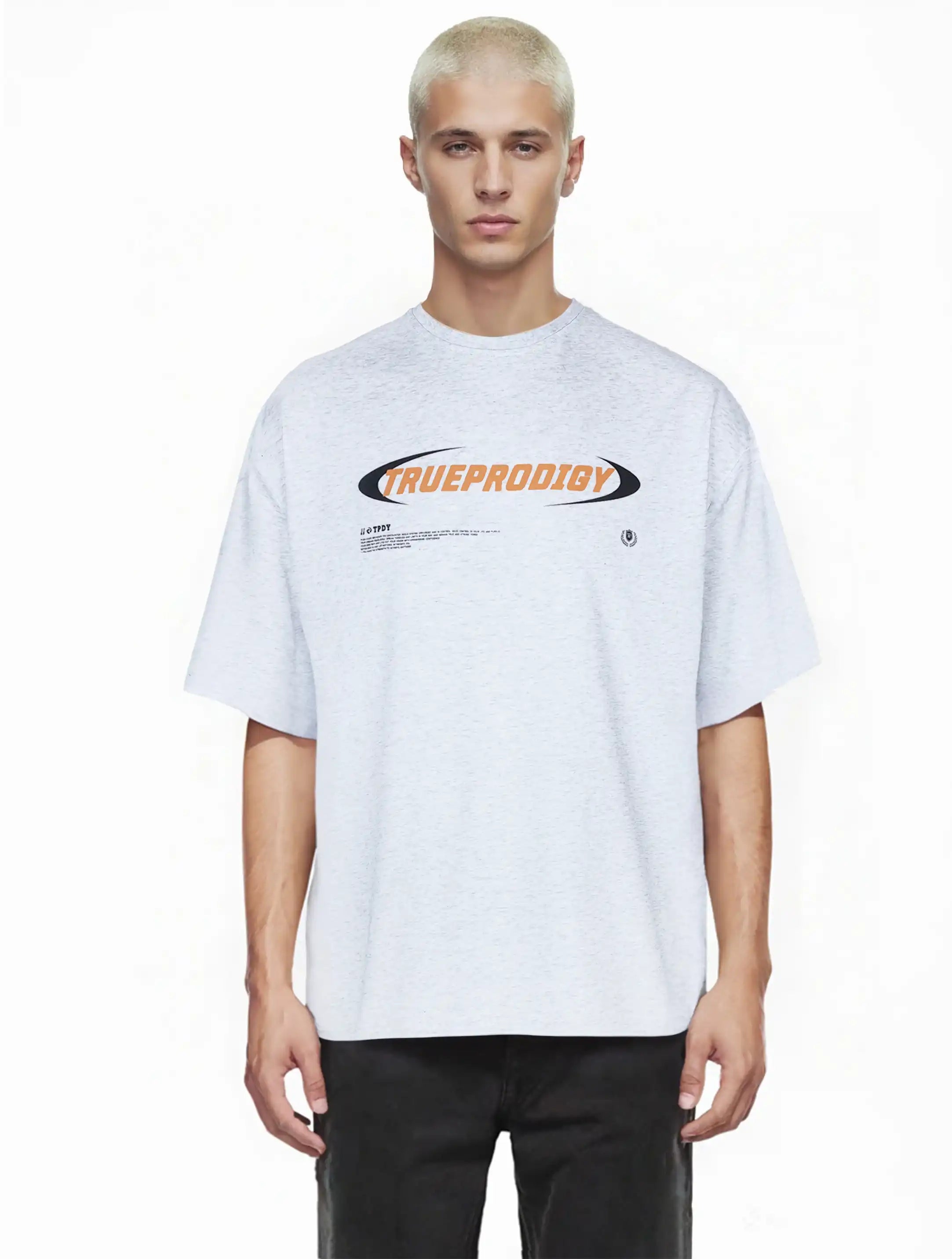 Eine Person mit kurzen, gebleichten blonden Haaren trägt das trueprodigy Oversize-Shirt mit großem trueprodigy-Schriftzug vorn in hellgrau mit schwarzer Hose, stehend vor einem schlichten weißen Hintergrund.