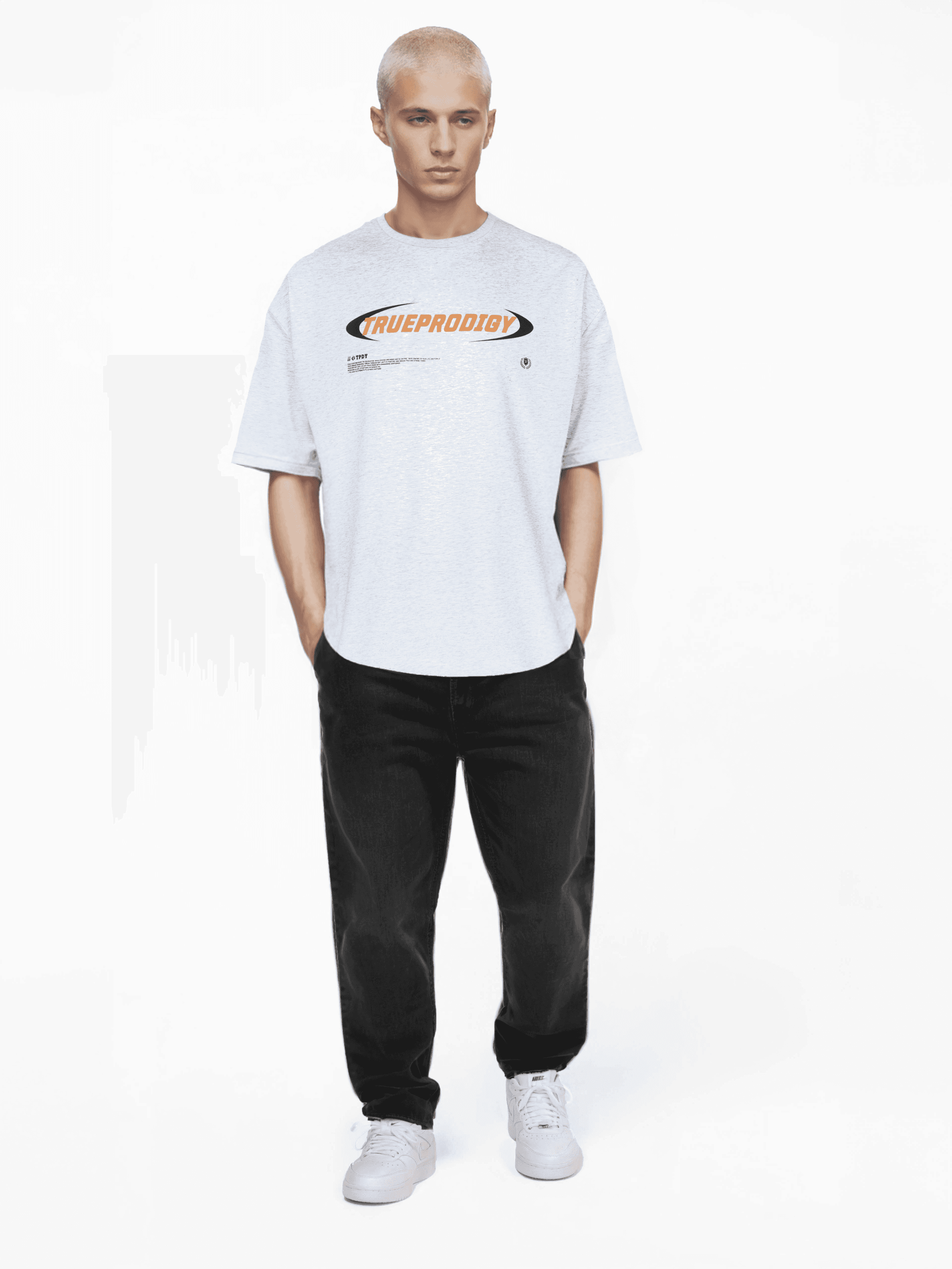 Eine Person mit kurzen blonden Haaren blickt nach vorne und trägt das übergroße hellgraue „Ravi“-T-Shirt von trueprodigy aus Jerseystoff mit Text und Grafiken, kombiniert mit schwarzen Hosen und weißen Turnschuhen vor einem schlichten weißen Hintergrund.