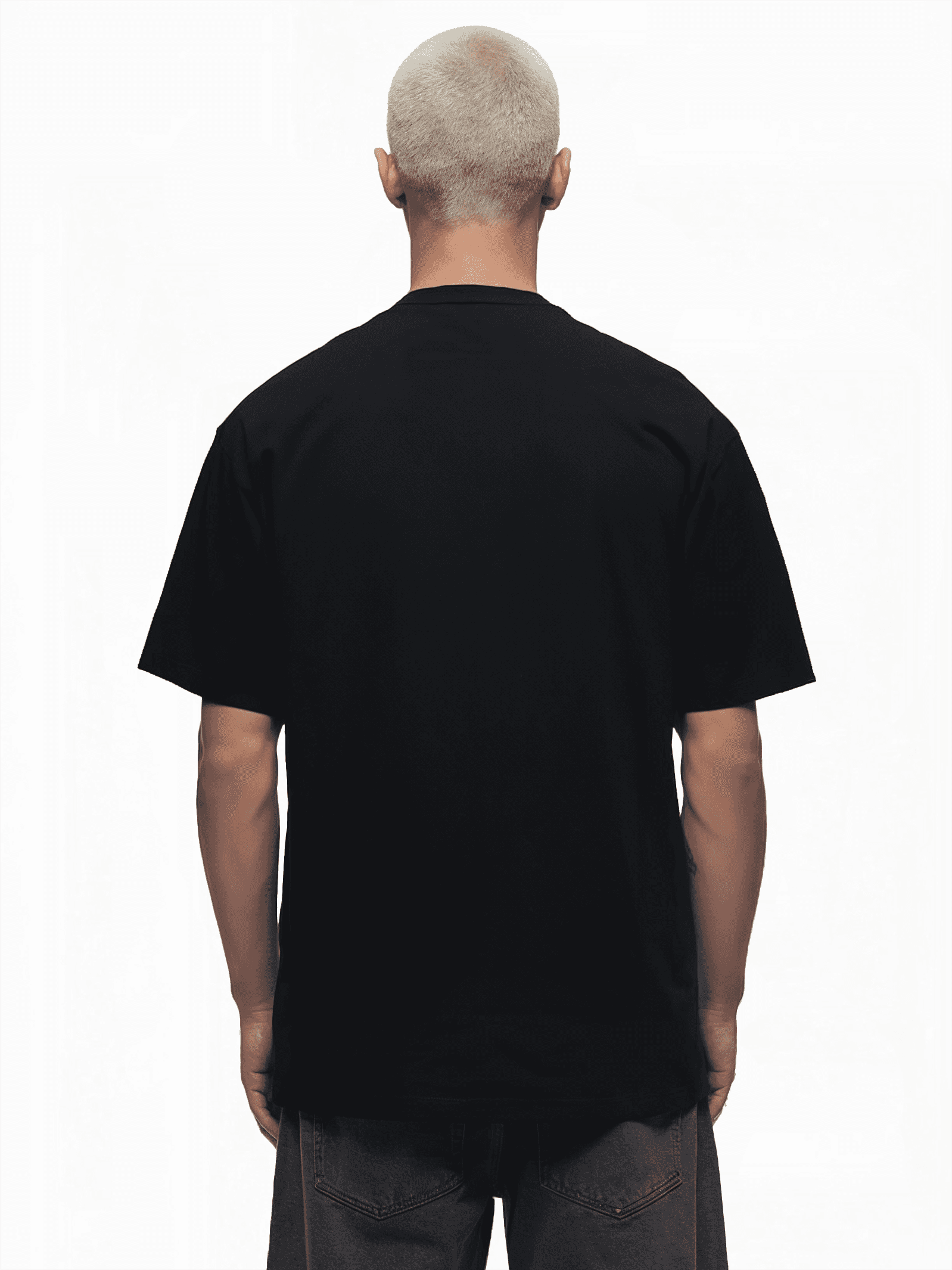 Eine Person mit kurzen, hellen Haaren blickt von der Kamera weg und hebt das trueprodigy Ravi Unisex-T-Shirt und die graue Hose hervor. Das schlichte schwarze Shirt hängt leicht übergroß vor einem strahlend weißen Hintergrund.