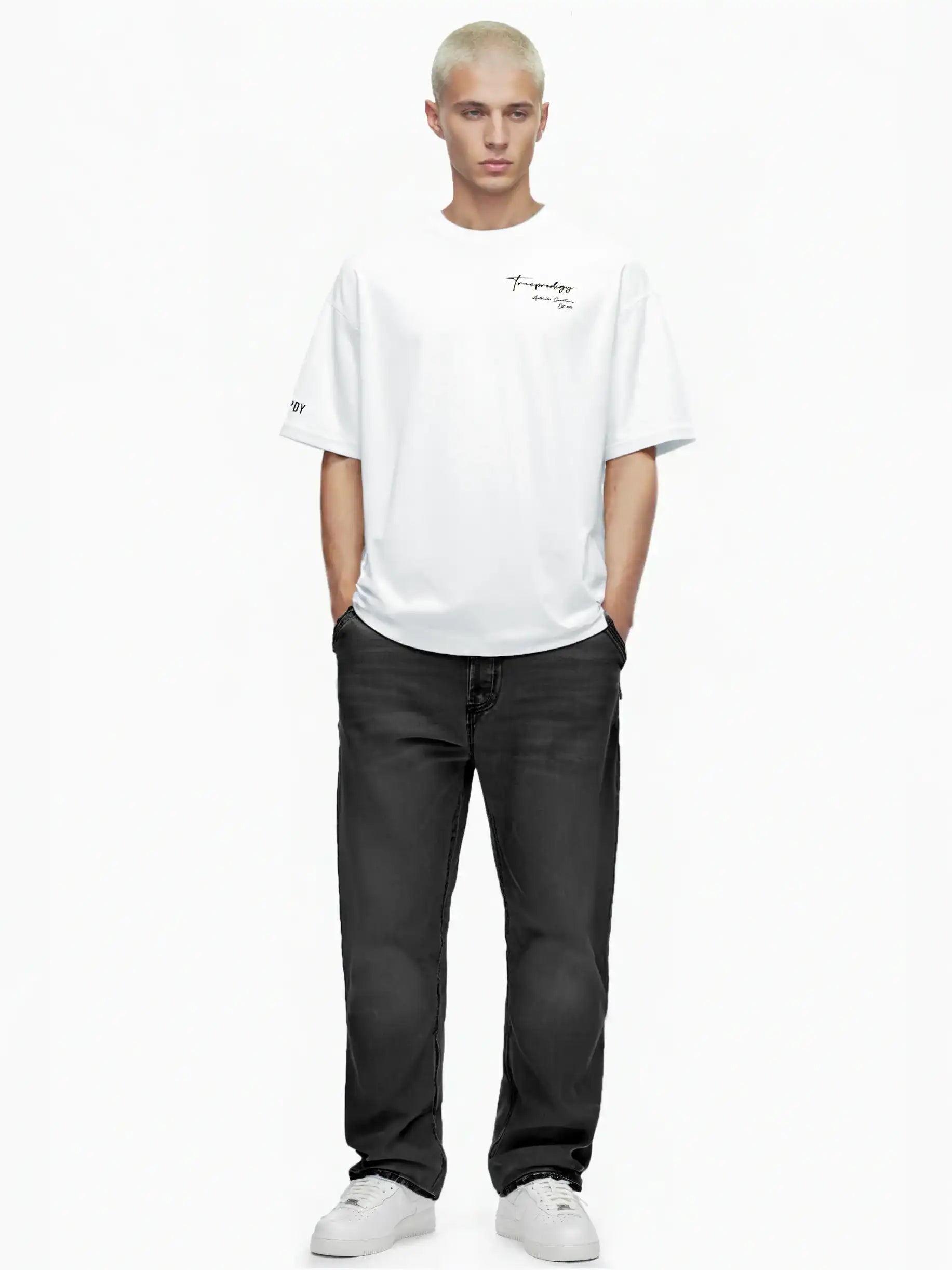 Eine Person mit kurzen blonden Haaren steht mit dem Gesicht nach vorne, trägt das trueprodigy Marin Oversize-T-Shirt mit edlem Schriftzug auf der Brust, schwarze Jeans und weiße Turnschuhe auf einem schlichten weißen Hintergrund. Die Hände sind in den Taschen.