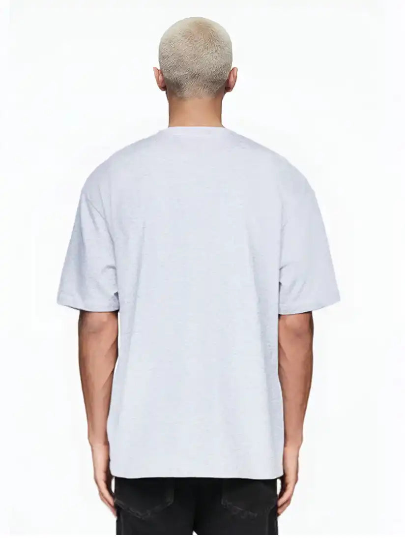 Eine Person mit kurzen, gebleichten blonden Haaren steht mit dem Rücken zur Kamera und trägt das trueprodigy Marin Oversize-T-Shirt mit edlem Schriftzug auf der Brust in hellgrau und schwarzer Hose vor einem schlichten weißen Hintergrund.