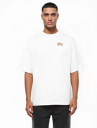 Ein Mann steht vor einem schlichten weißen Hintergrund und trägt das trueprodigy Oversize-Shirt mit TPDY-Logo & Rückenprint "Stay Real" in schwerem Jerseystoff und schwarzer Hose.
