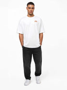 Ein Mann blickt nach vorne und trägt ein weißes trueprodigy Oversize-Shirt mit TPDY-Logo & Rückenprint "Stay Real", schwarze Jeans und weiße Turnschuhe. Er hat die Hände in den Taschen und steht vor einem schlichten weißen Hintergrund.