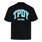 Das trueprodigy Oversize-Shirt mit TPDY-Logo ist ein schwarzes Unisex-Shirt aus schwerem Jerseystoff mit großen hellblauen TPDY-Blockbuchstaben vorne und weißem "Stay Real"-Rückenprint.