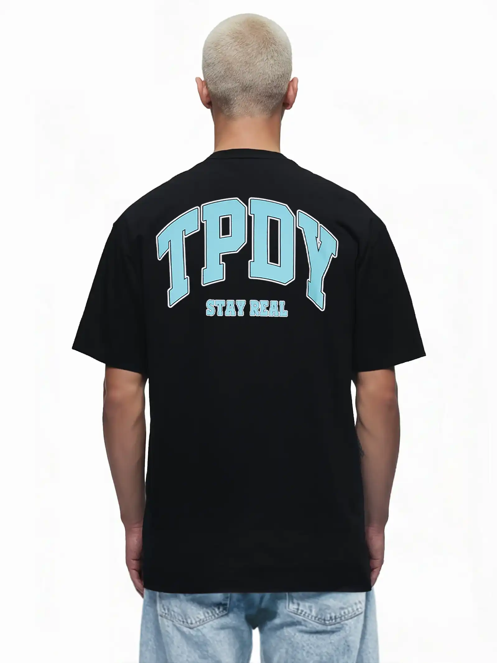 Eine Person mit kurzen, gebleichten Haaren ist von hinten zu sehen, die das trueprodigy Oversize-Shirt mit TPDY-Logo & Rückenprint "Stay Real" in Schwarz trägt, gestylt mit hellblauen Jeans.
