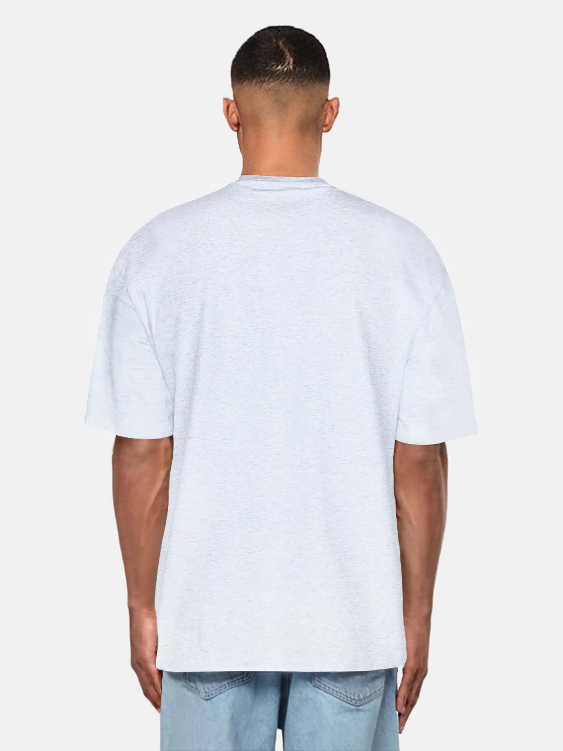 Ein Mann steht mit dem Rücken zur Kamera, trägt ein hellgraues trueprodigy Oversize-Herren-T-Shirt mit Logo-Smile-Grafik auf der Brust und hellblaue Denim-Shorts vor einem schlichten weißen Hintergrund.