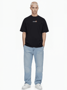 Vor einem weißen Hintergrund steht eine kleine, blonde Person, die ein Trueprodigy Unisex Oversize „Juniper“-T-Shirt aus Jerseystoff trägt, dazu hellblaue Jeans und weiße Sneakers, und die Hände lässig in die Hosentaschen steckt.