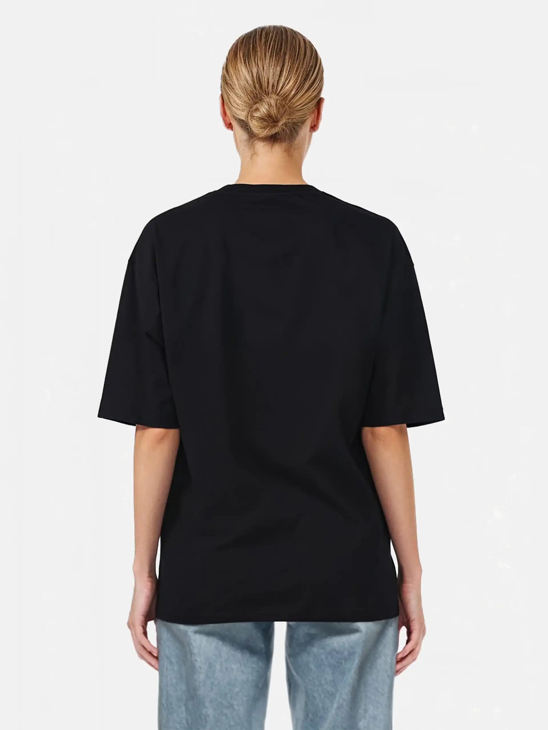 Gezeigt wird eine Person mit blondem Haar in einem tiefen Dutt von hinten, die ein trueprodigy Juniper F Oversize-Damen-T-Shirt mit Logo-Smile-Grafik auf der Vorderseite und hellblaue Jeans vor einem schlichten weißen Hintergrund trägt.