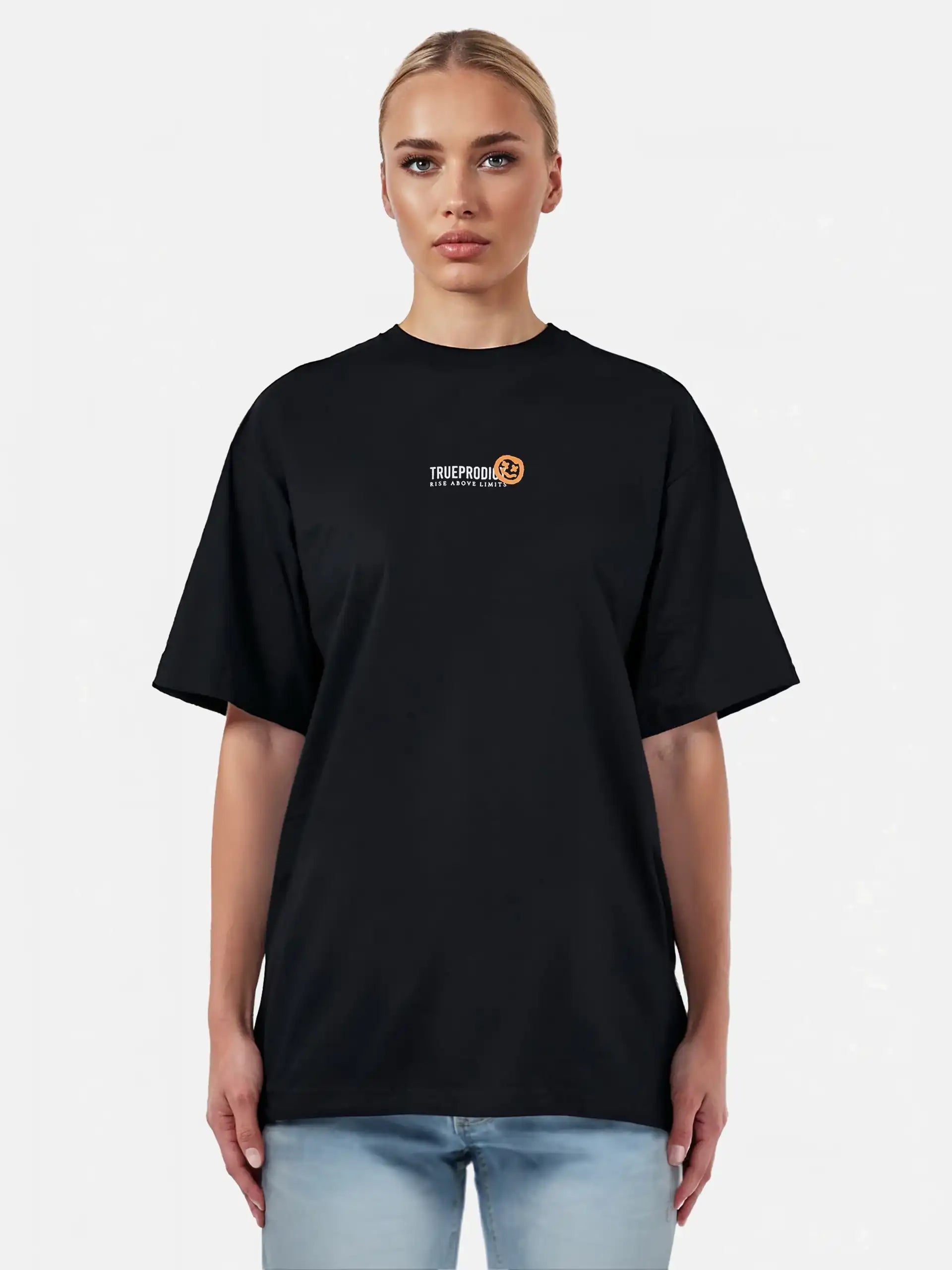 Eine Person mit hellen, zurückgegelten Haaren trägt ein schwarzes trueprodigy Juniper F Oversize-Damen-T-Shirt mit einer Logo-Smile-Grafik auf der Vorderseite, gepaart mit hellblauen Jeans, vor einem schlichten hellen Hintergrund.