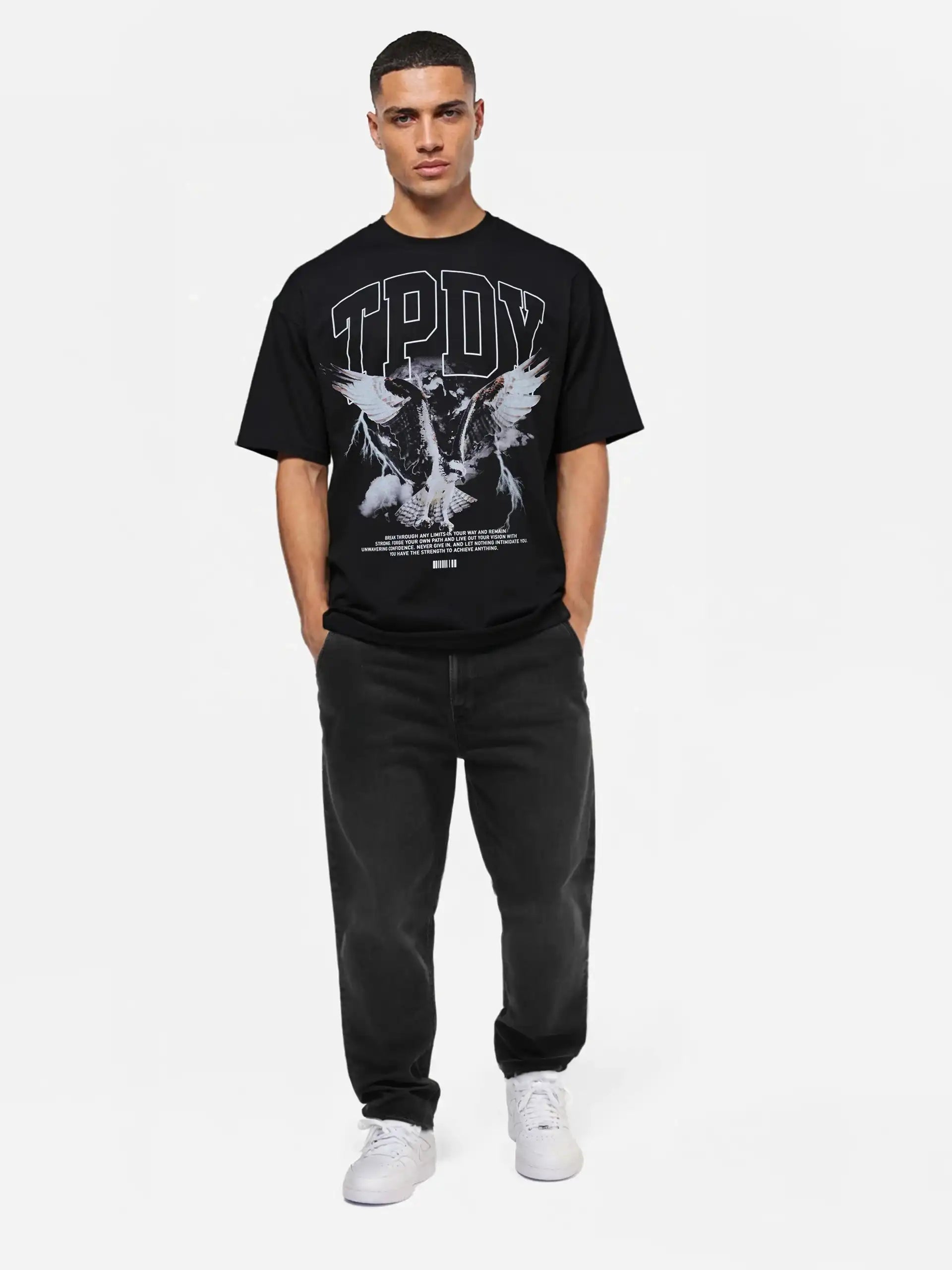 Eine Person steht vor einem weißen Hintergrund und trägt das trueprodigy Yuki Oversize-T-Shirt mit Adlergrafik & TPDY-Schriftzug in Schwarz, gepaart mit schwarzen Jeans und weißen Sneakers.