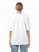 Eine Person mit blondem Dutt blickt abgewandt und trägt ein übergroßes Trueprodigy Yuki F T-Shirt und hellblaue Jeans. Das schlichte weiße Unisex-T-Shirt ergänzt den minimalistischen Hintergrund.