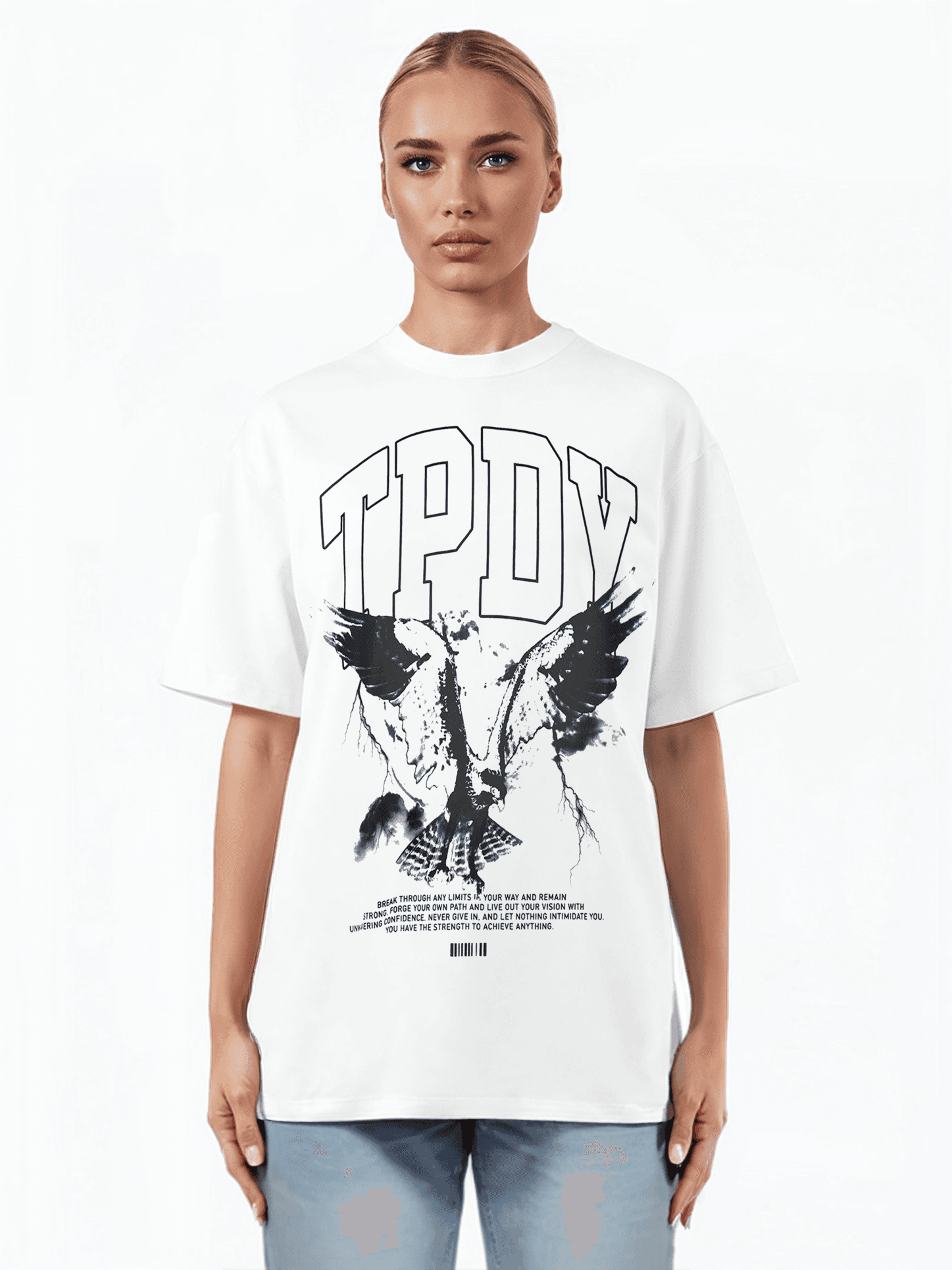 Eine Person steht vor einem schlichten weißen Hintergrund und trägt das TrueProdigy Yuki F Unisex T-Shirt mit dem Schriftzug „TPDY“ oben und einem kunstvollen Adlermotiv darunter. Der übergroße Schnitt passt perfekt zu den zurückgekämmten Haaren und der hellblauen Jeans.