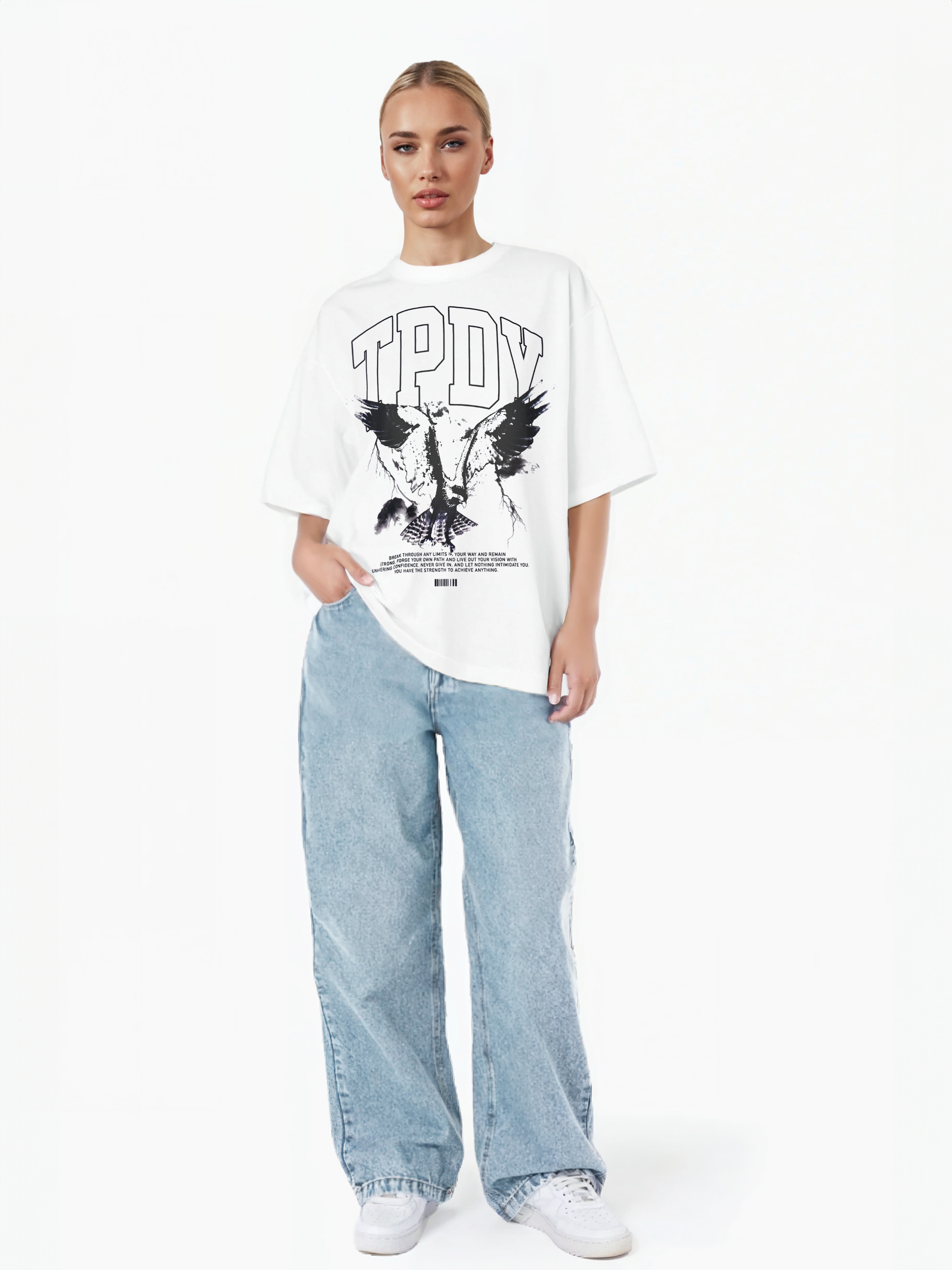 Eine Person steht vor einem weißen Hintergrund und trägt ein weißes trueprodigy Oversize-T-Shirt mit Adlergrafik & TRUEPRODIGY-Schriftzug, lockere hellblaue Jeans und weiße Turnschuhe. Eine Hand steckt in ihrer Tasche.