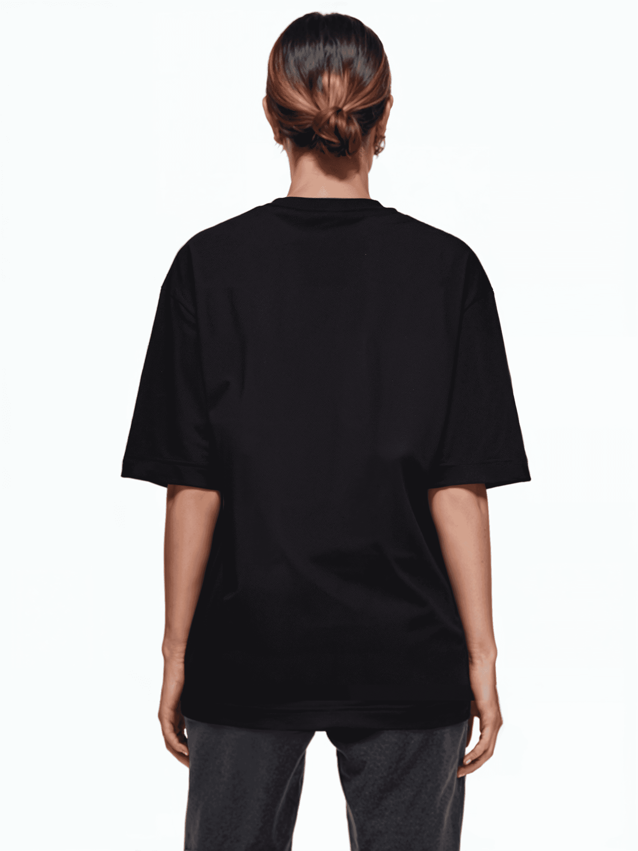 Eine Person mit zurückgebundenem Haar, die ein schwarzes Unisex-T-Shirt von Trueprodigy Yuki F und dunkle Hosen trägt, blickt von der Kamera ab und steht vor einem schlichten weißen Hintergrund, der das elegante Design des Outfits hervorhebt.